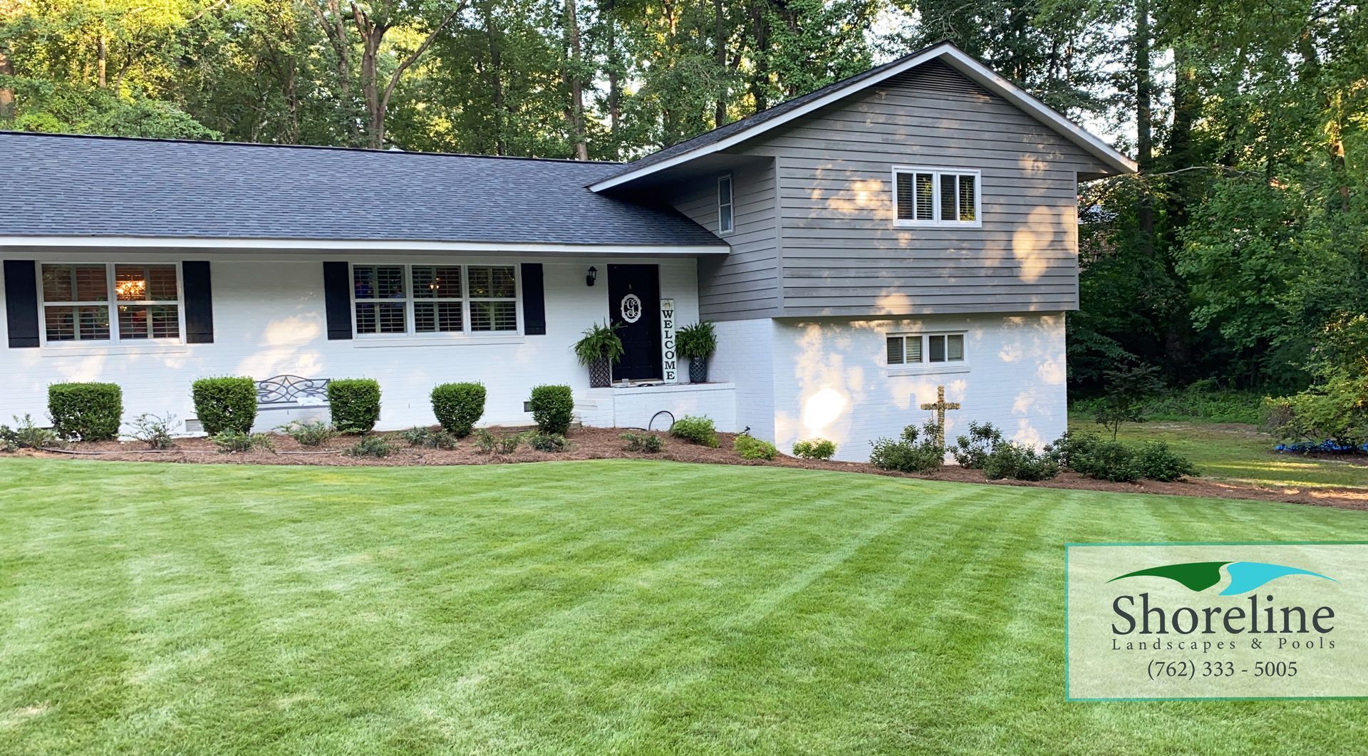 White house with black accents, front lawn with recently cut grass, and greenery.