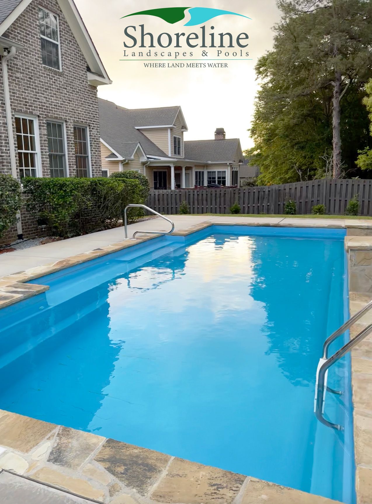 Rectangular blue swimming pool in a residential backyard, with a house in the background.