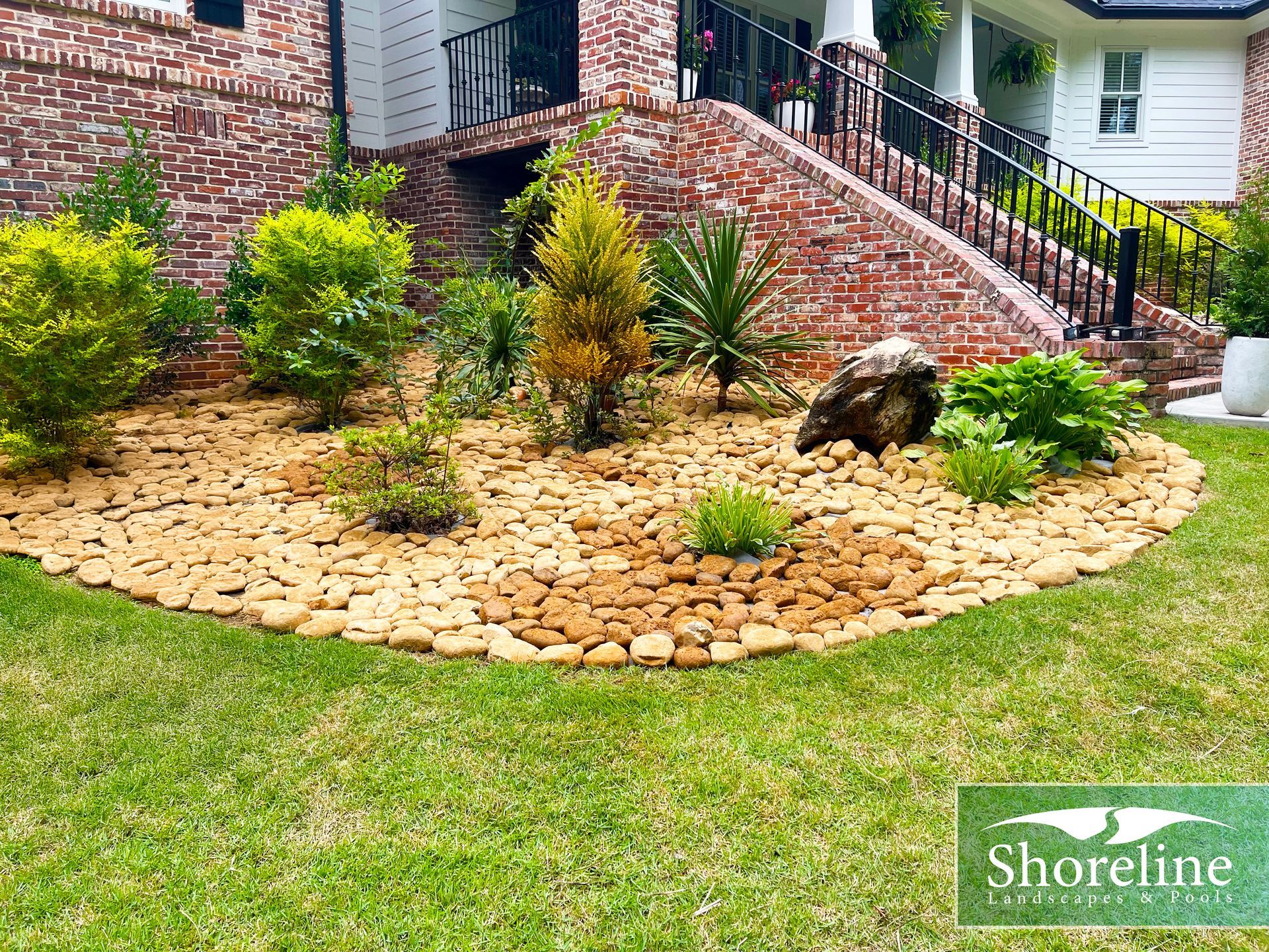 Landscaped garden bed with rocks, plants, and brick house.