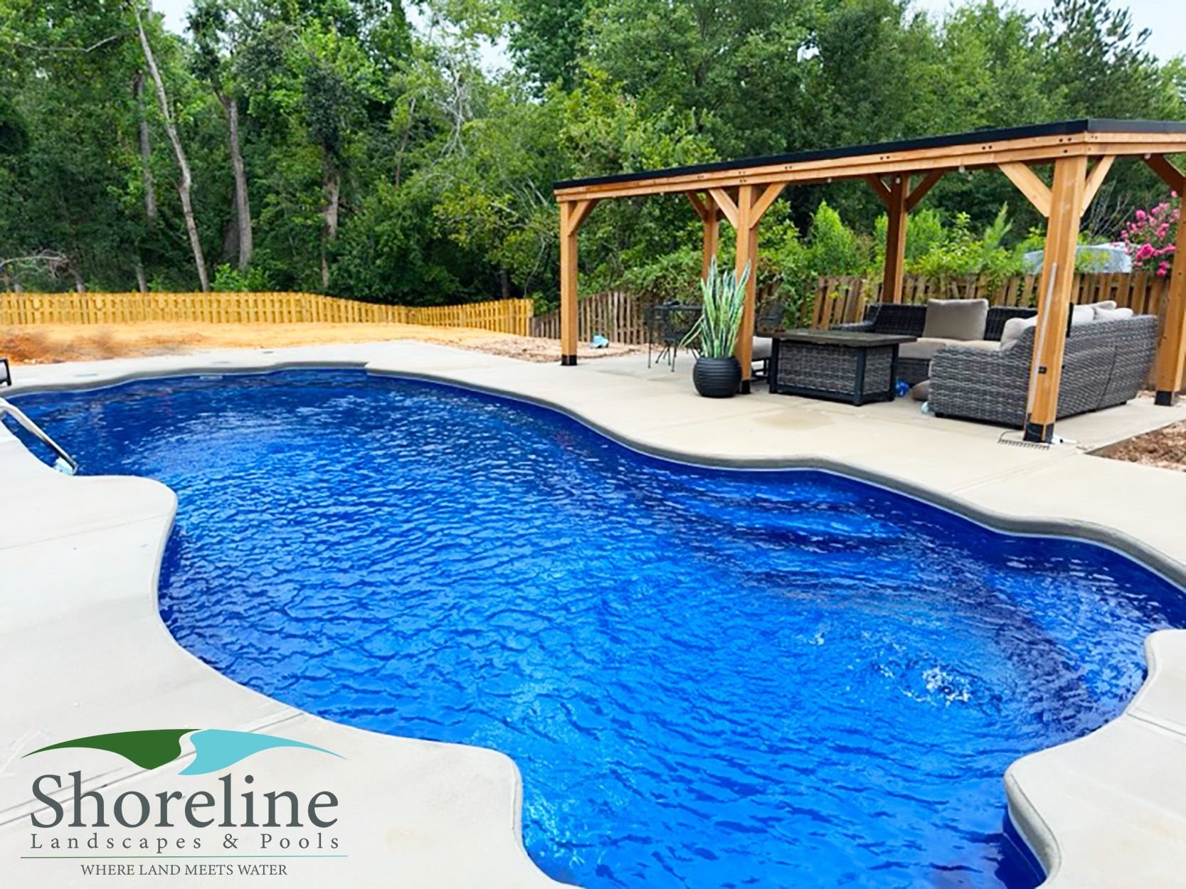 Pool with blue water and pergola with seating; Shoreline Landscapes & Pools logo.