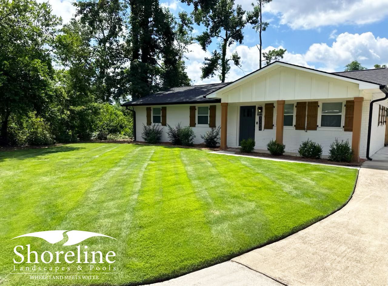 Well-manicured lawn in front of a white house with brown shutters and wooden posts.