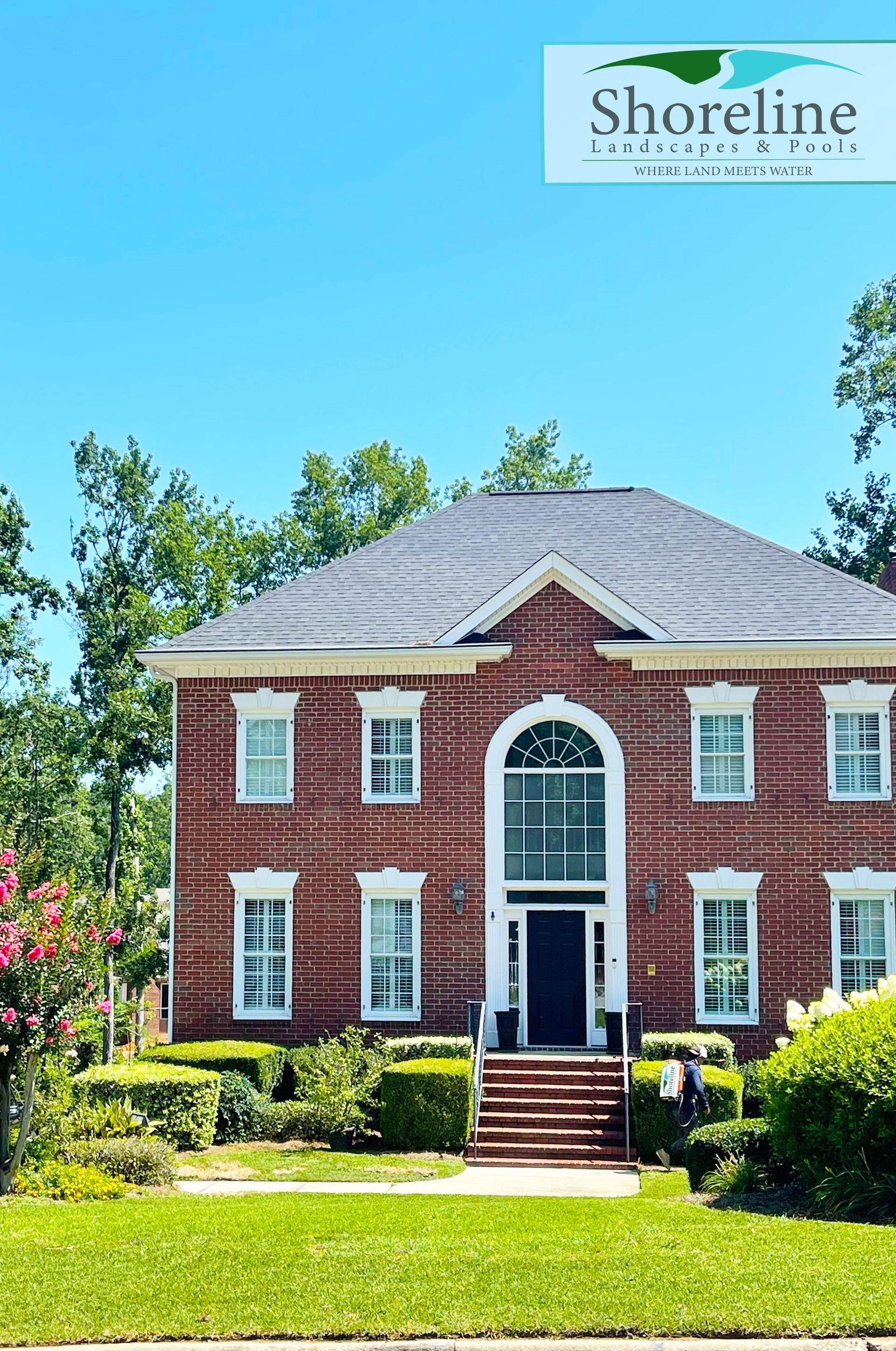 Two-story brick house with white trim, dark blue door, and arched window under a blue sky.