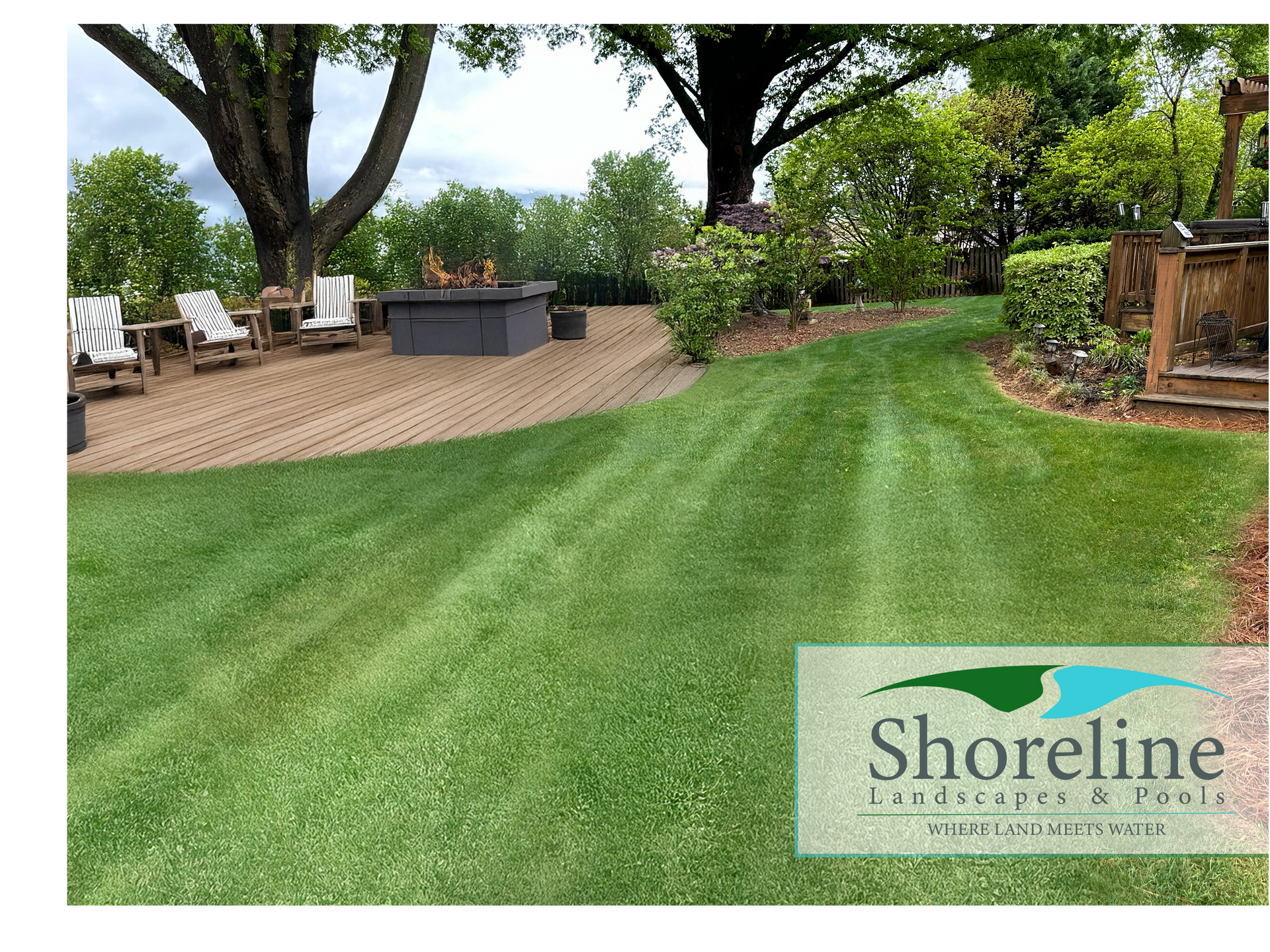 Lush green lawn with a patio, fire pit, and trees in the background, promoting Shoreline Landscapes & Pools.