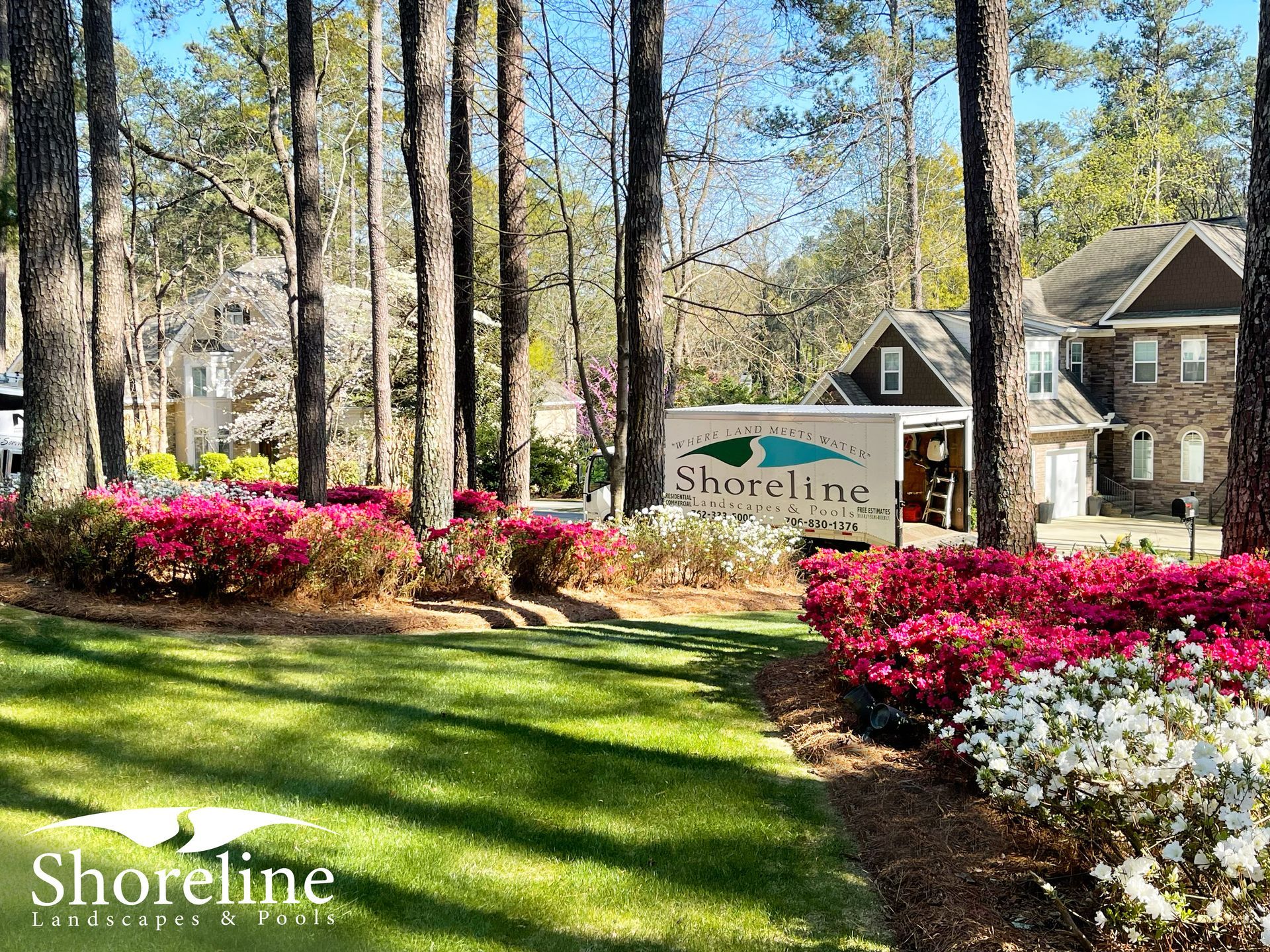 Shoreline landscaping truck parked near pink and white azaleas in a residential area.