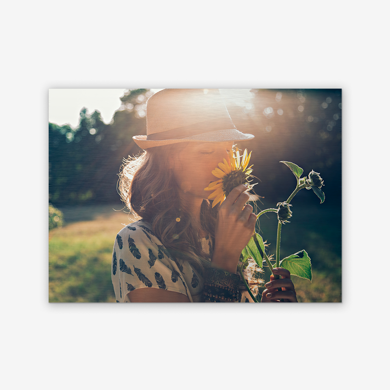 A woman in a hat is smelling a sunflower.