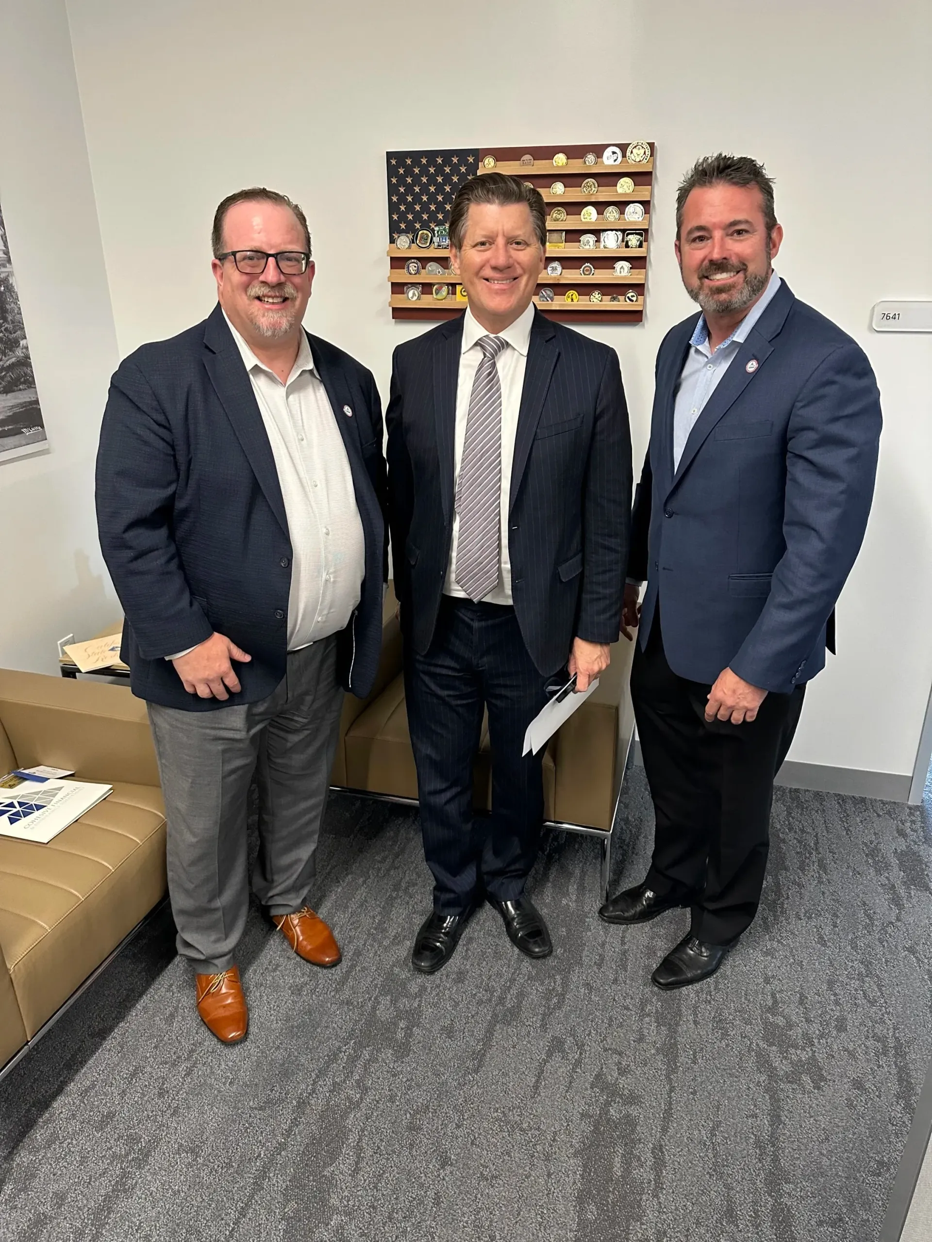 Three men in suits and ties are posing for a picture in a room.