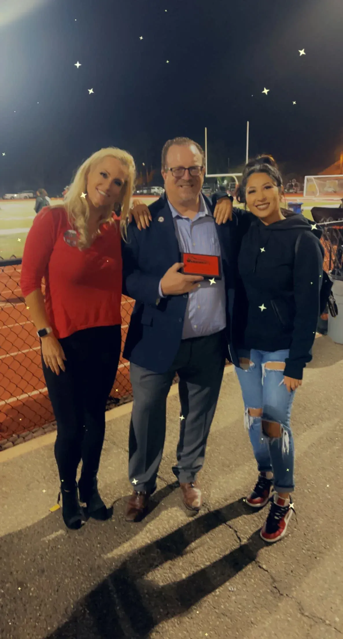 A man and two women are standing next to each other on a football field.