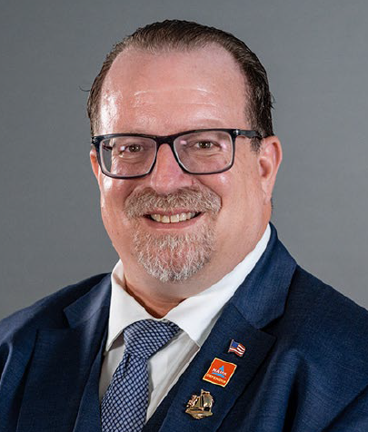 A man with glasses and a beard is wearing a suit and tie.