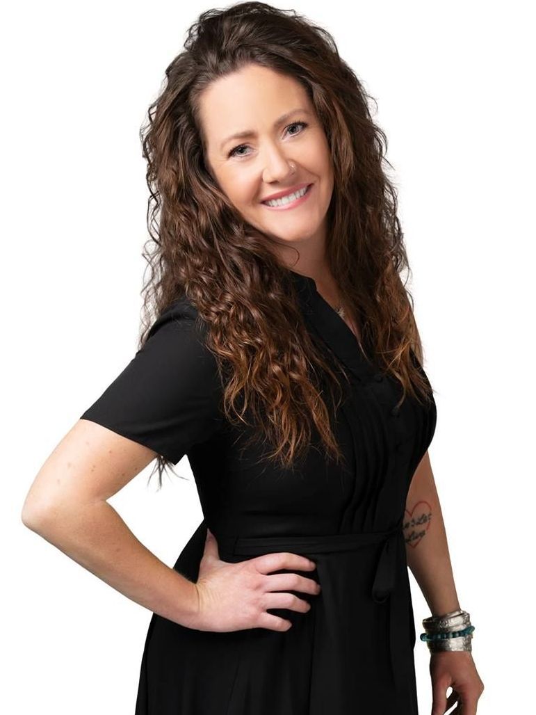 A woman in a black dress is standing with her hands on her hips and smiling.