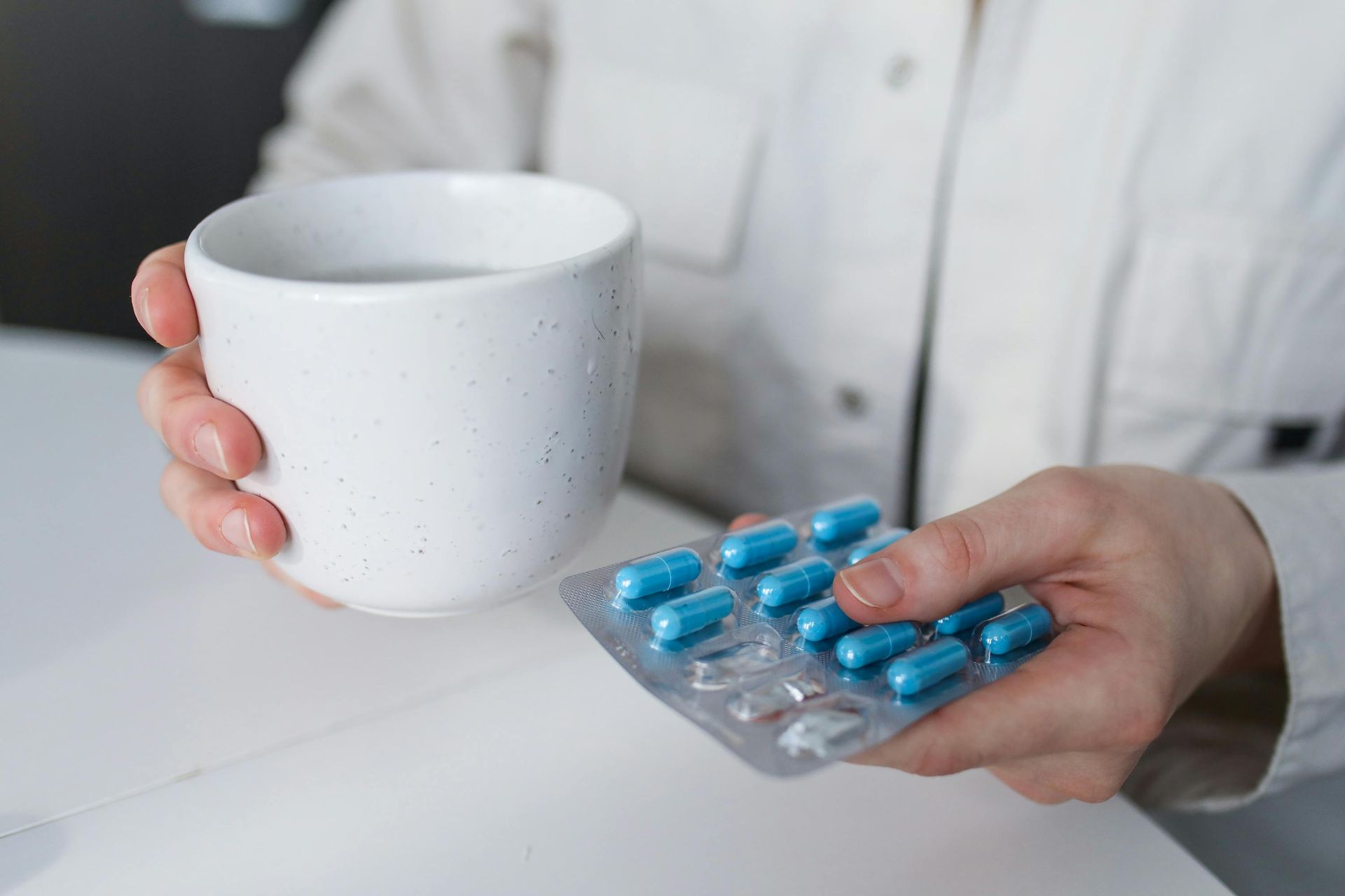 A person is holding a cup of coffee and a blister pack of pills.