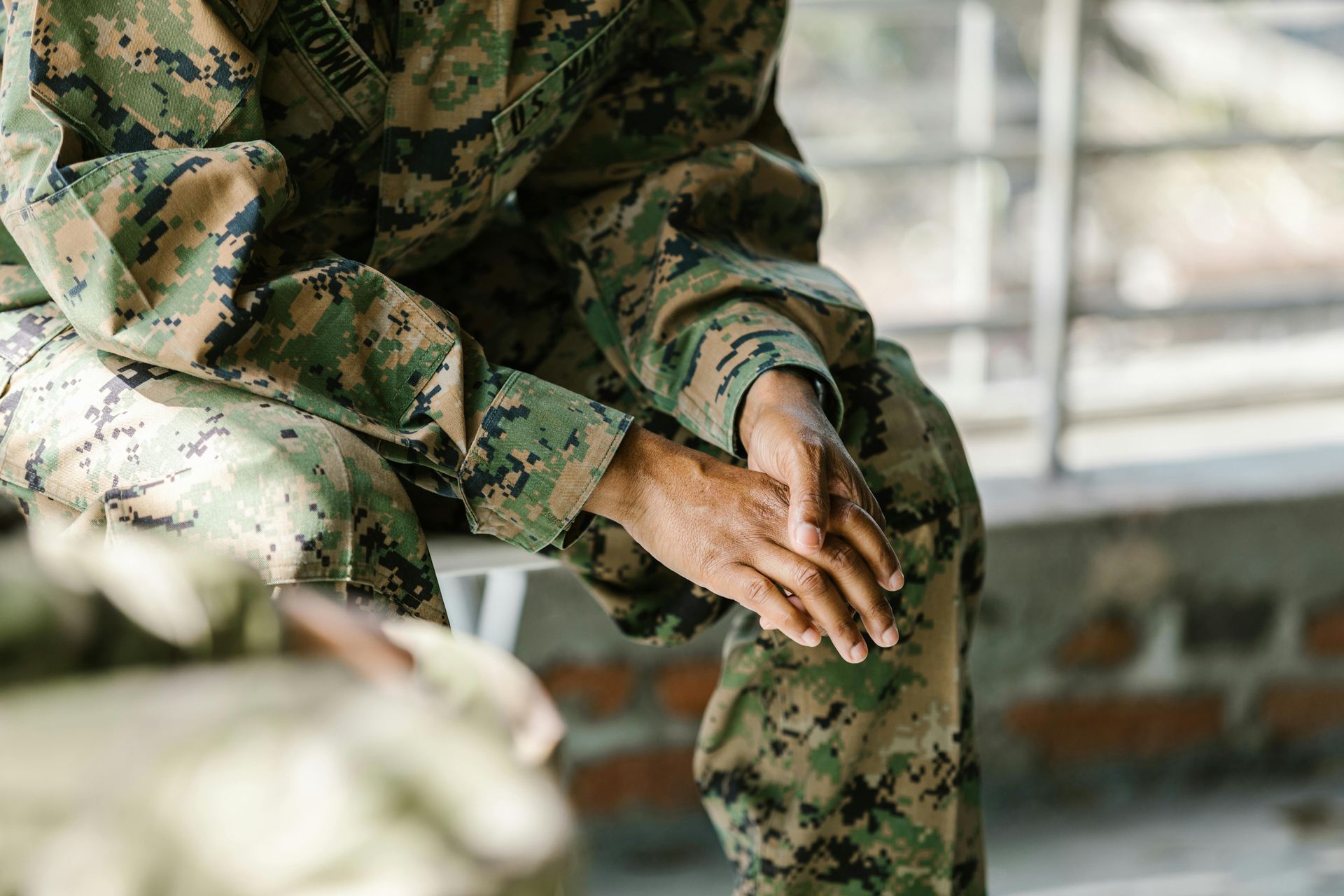 A soldier is sitting on a bench with his hands on his knees.