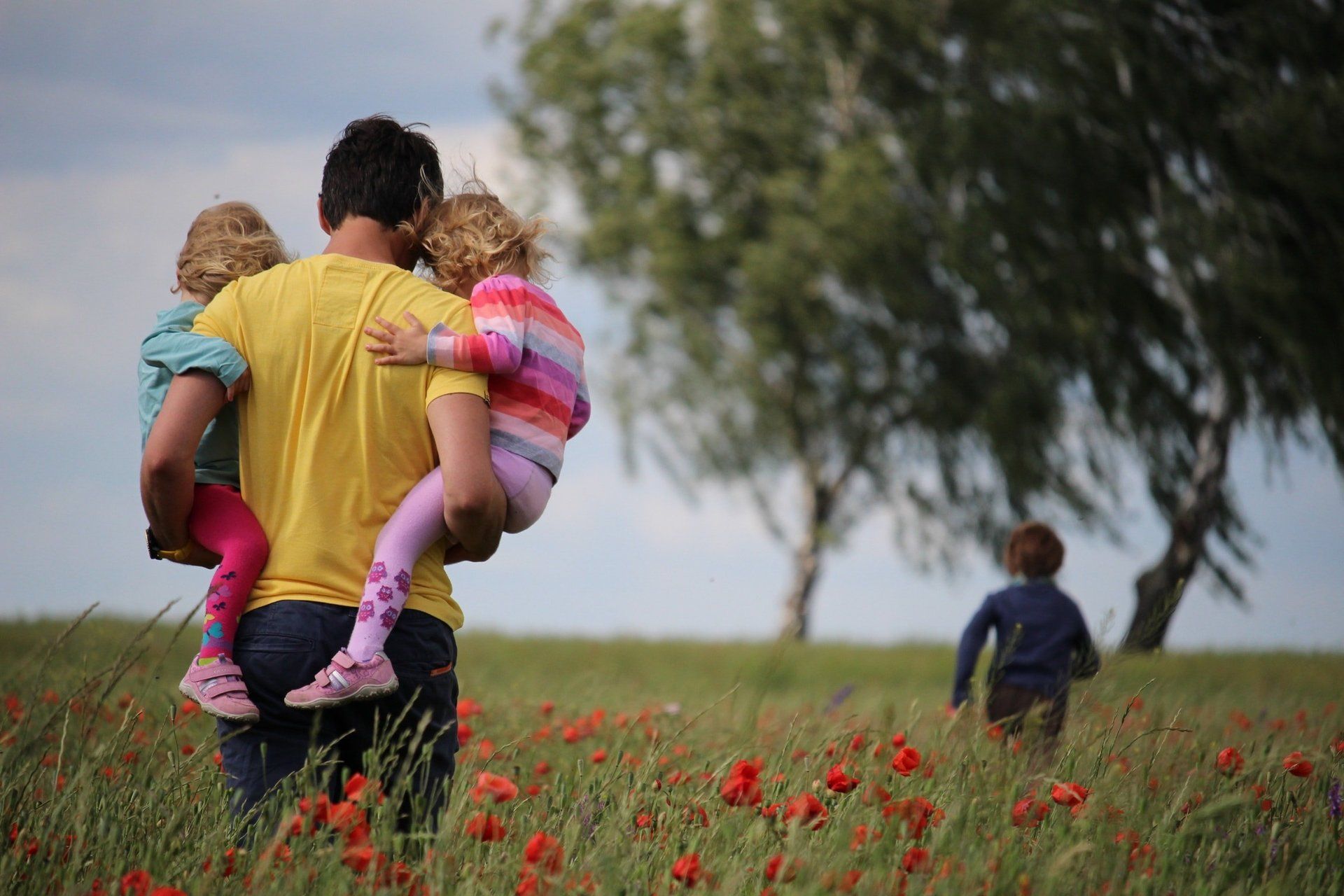 A man carrying two children in a field of flowers