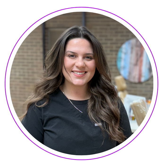 Smiling Sierra M. with long wavy brown hair, wearing a black shirt, at the Small and Piers dental practice.
