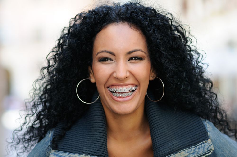 A woman with curly hair and braces is smiling and wearing hoop earrings.