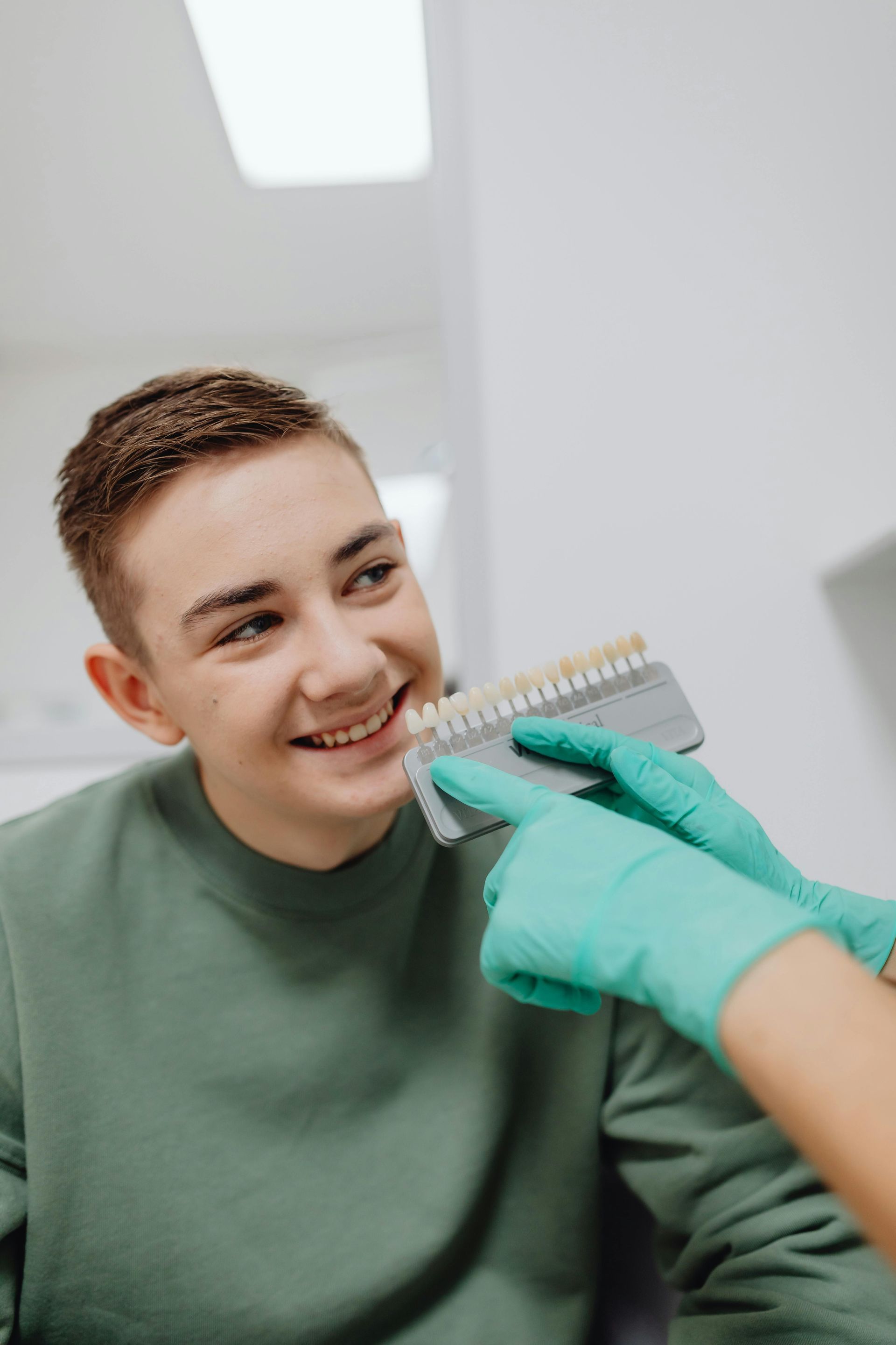 Person at a dentist, comparing tooth color to a shade guide held by gloved hands.