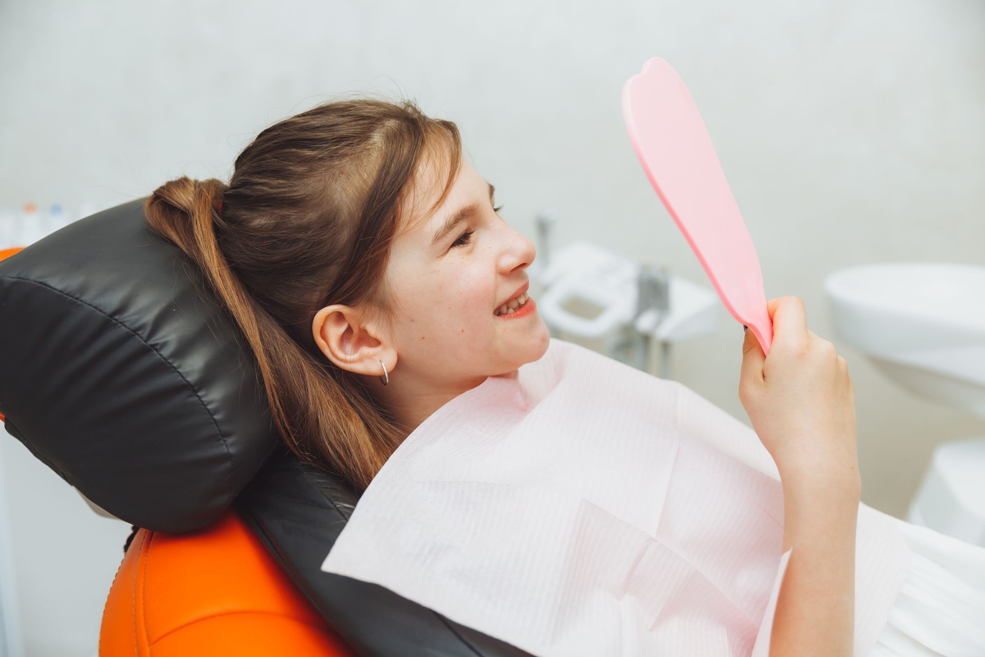 Dentist reclining with a pink mirror, smiling and wearing a bib during a dental exam