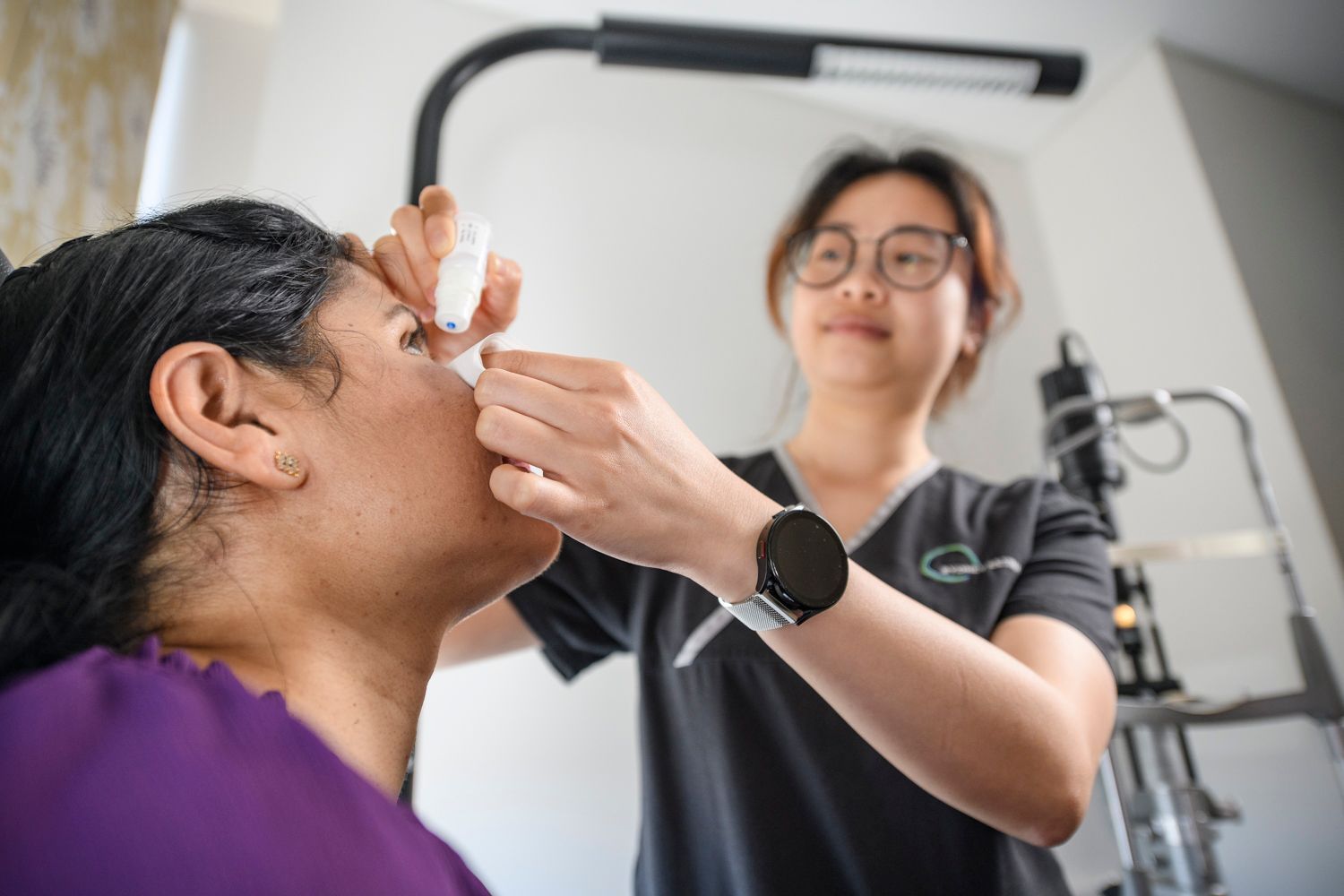 Optometrist administering eye drops to a patient in an exam room.