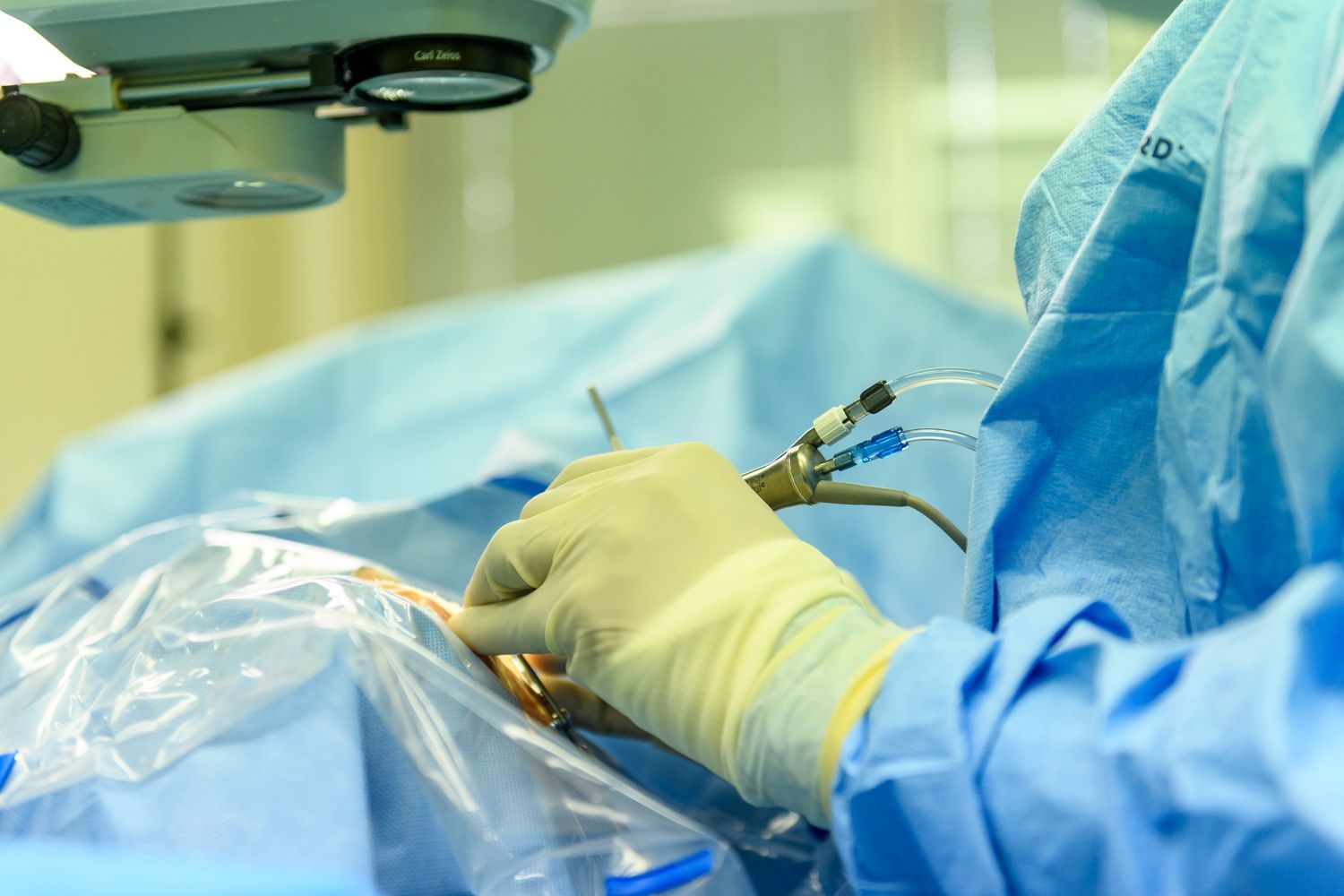 Surgeon in blue scrubs and gloves performing surgery, with medical instruments and equipment.