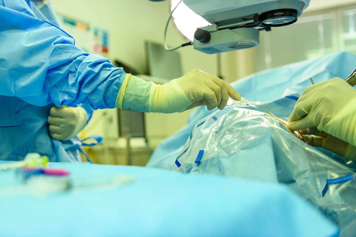 Surgeons in blue scrubs operating in a sterile surgical room, using tools on a patient covered in blue drapes.