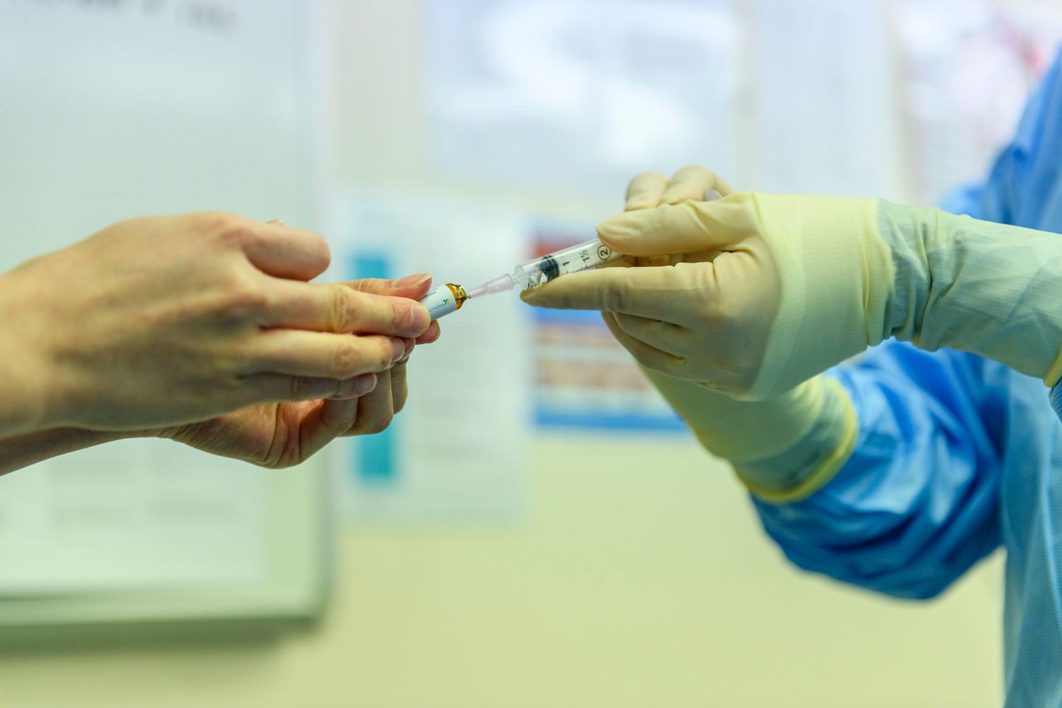 Person in medical scrubs filling syringe from vial with gloved hands.