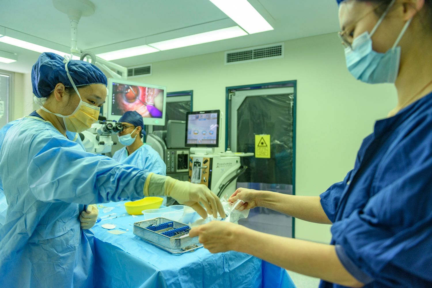 Medical staff in an operating room preparing instruments, wearing surgical attire, illuminated by overhead lights.