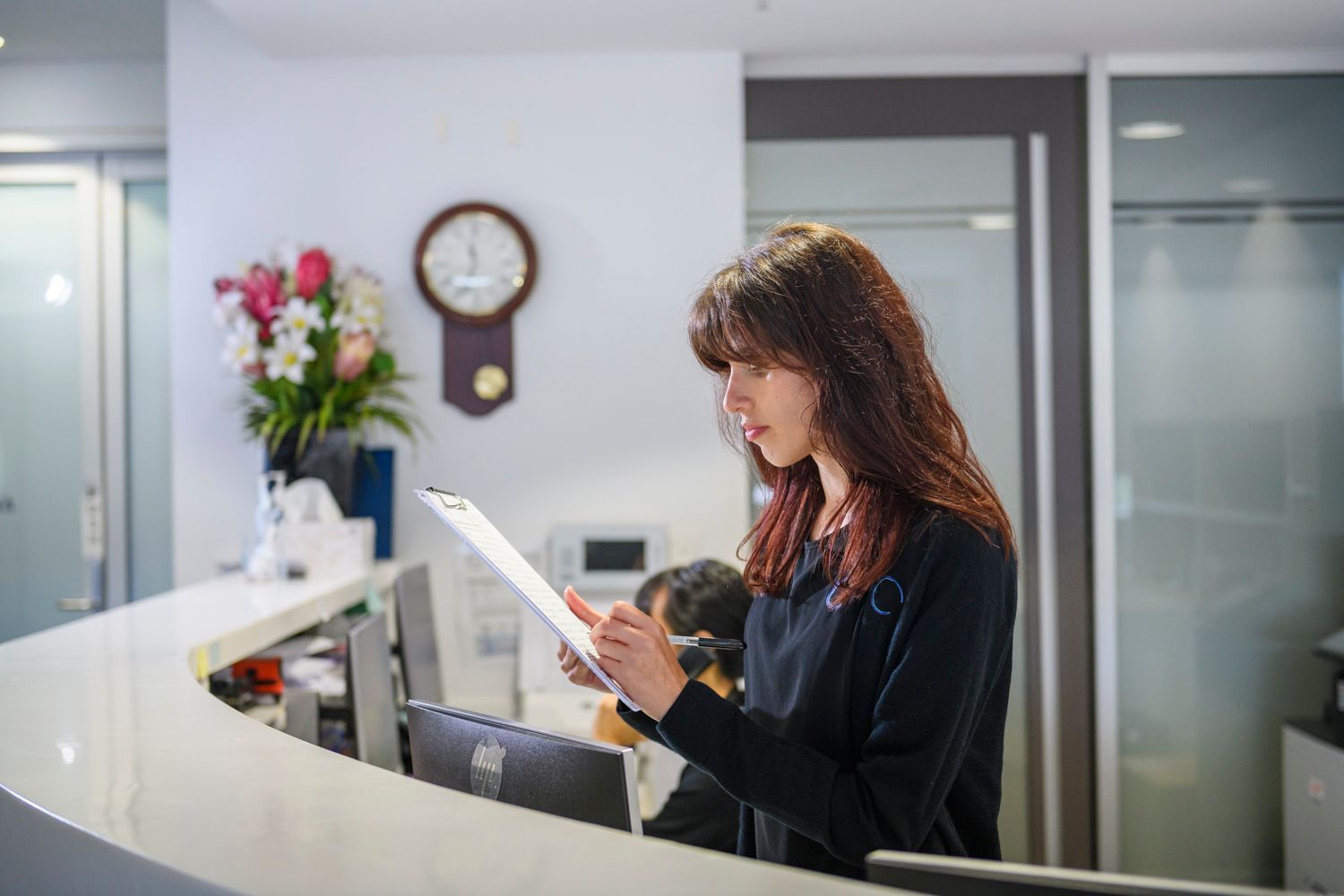 Woman reviewing document at a reception desk in a brightly lit office.