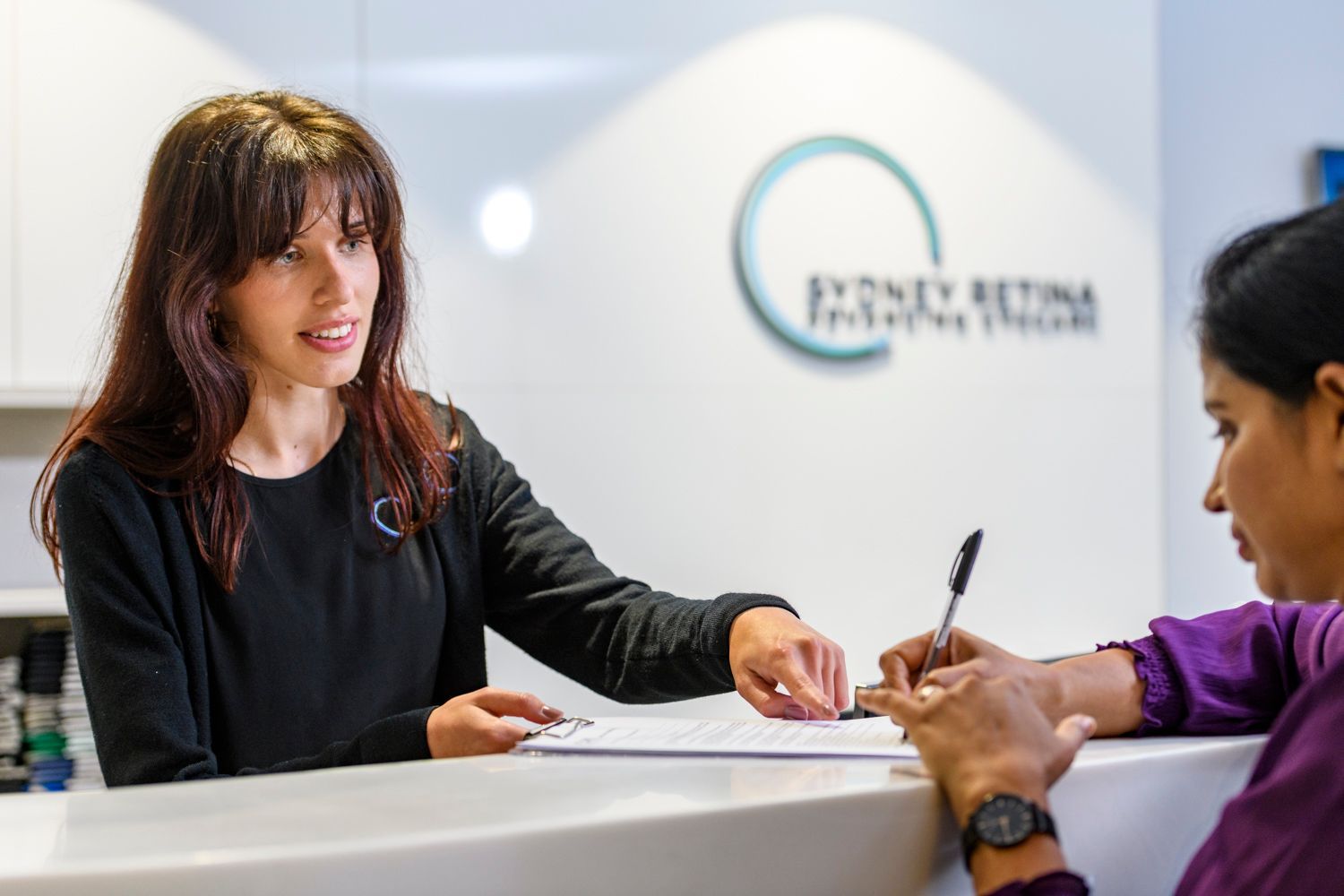 Receptionist helping a patient with paperwork at a retina clinic's reception desk.
