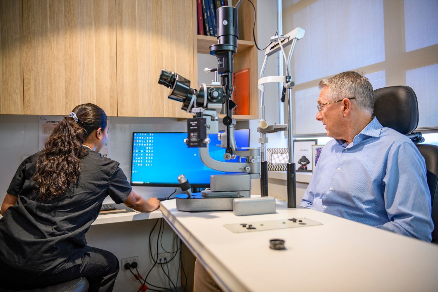 Optometrist examining a patient's eyes using a slit lamp in an office setting.