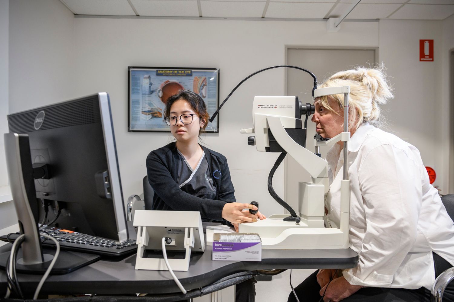 Optometrist examining a patient's eyes with specialized equipment in a clinic setting.