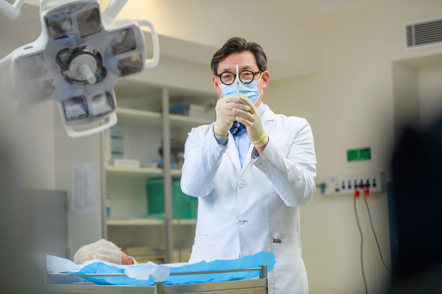 Doctor in surgical mask and gloves, holding a syringe, preparing for an injection. Operating room setting.