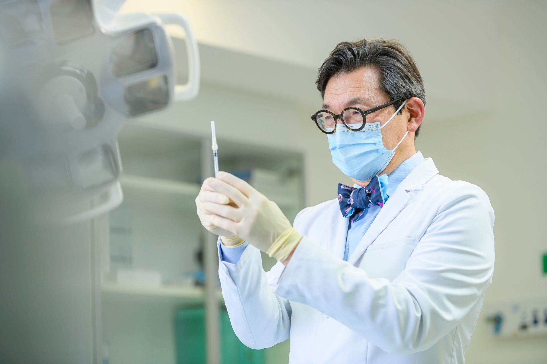 Doctor in a white coat, mask, and bow tie, holding a syringe, preparing for an injection.