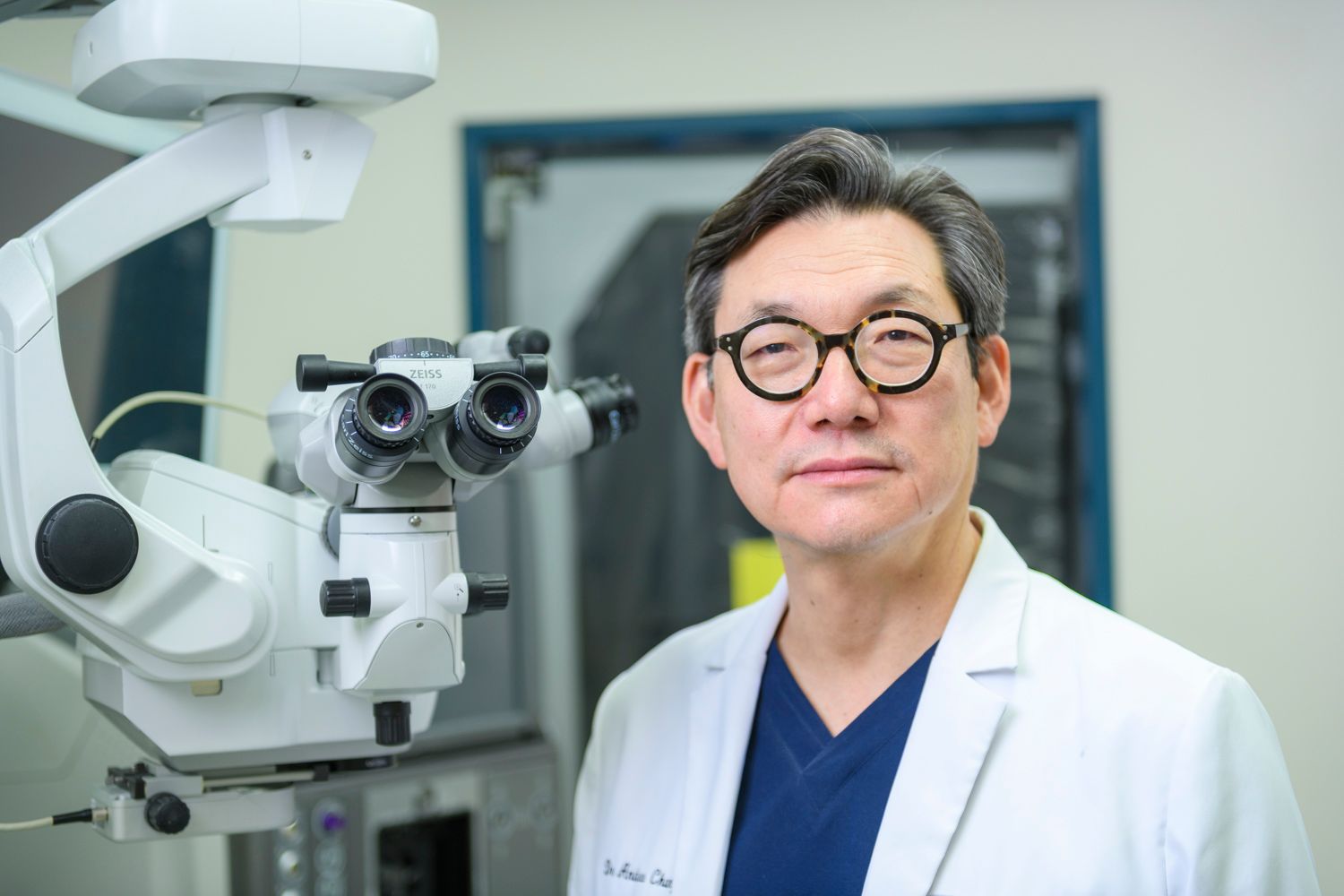 Doctor in lab coat poses near surgical microscope.