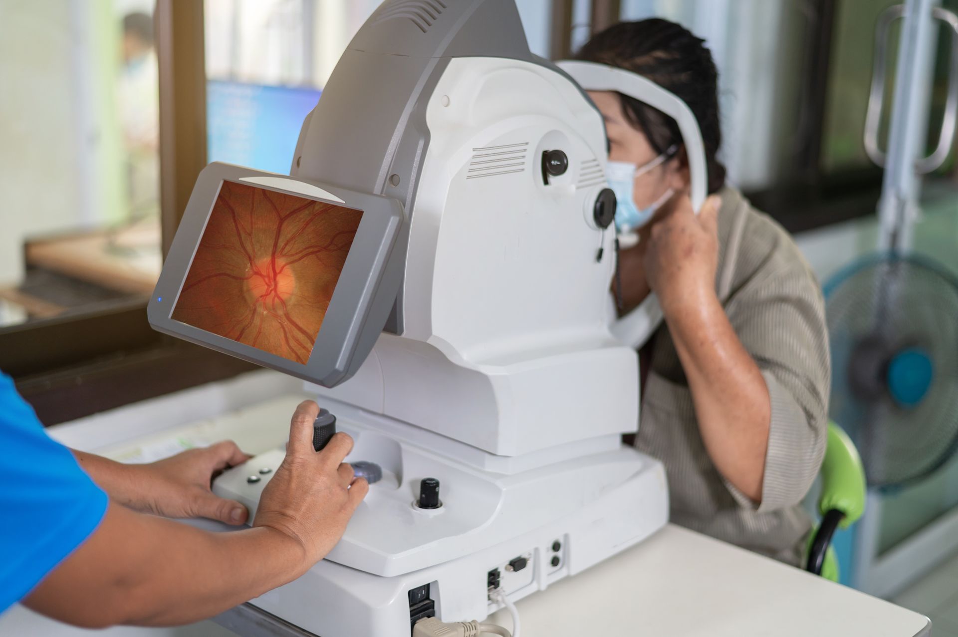 Woman undergoing eye exam with retinal imaging machine; doctor operating the device.