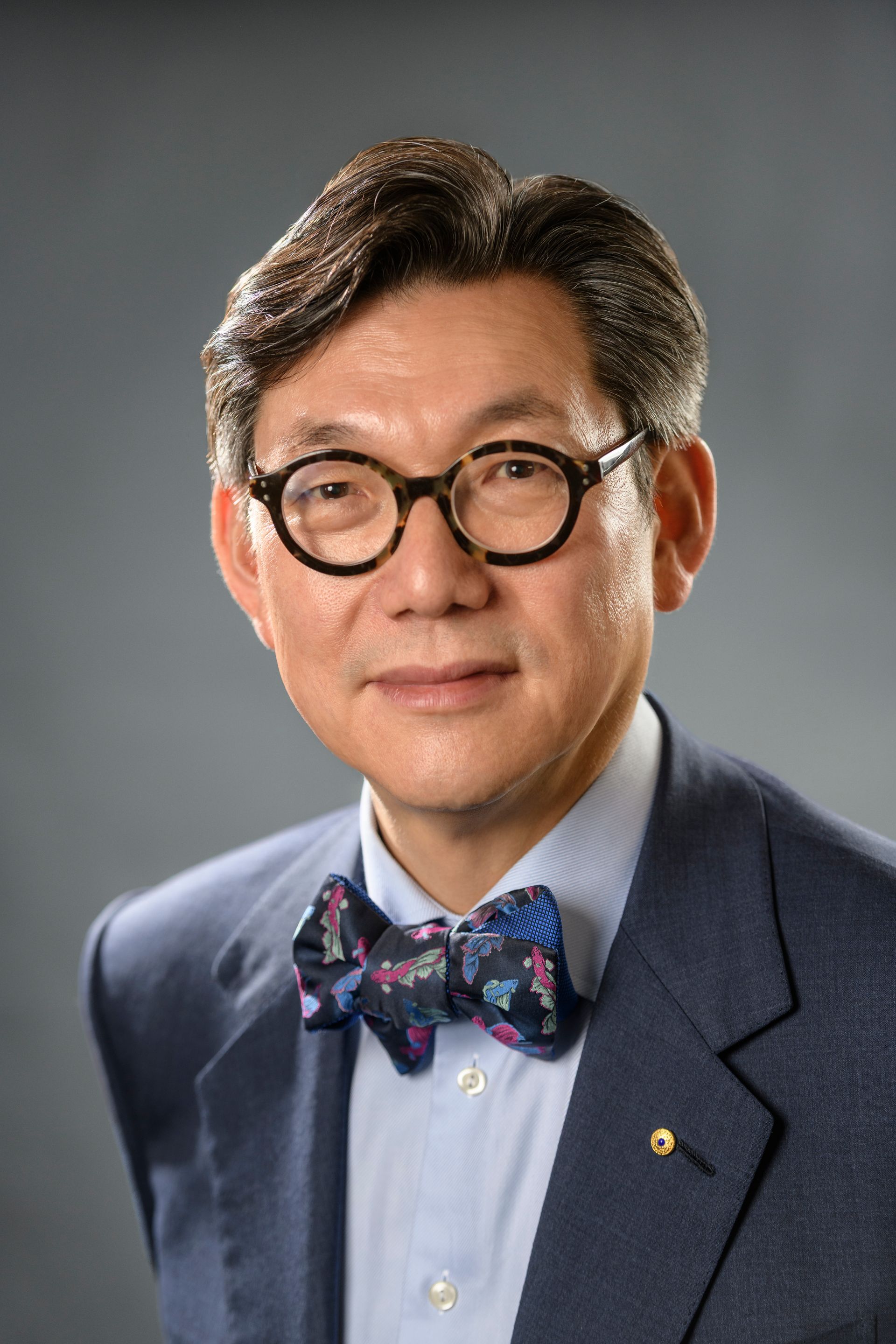 Man wearing glasses and a bow tie, facing forward, against a light gray background.