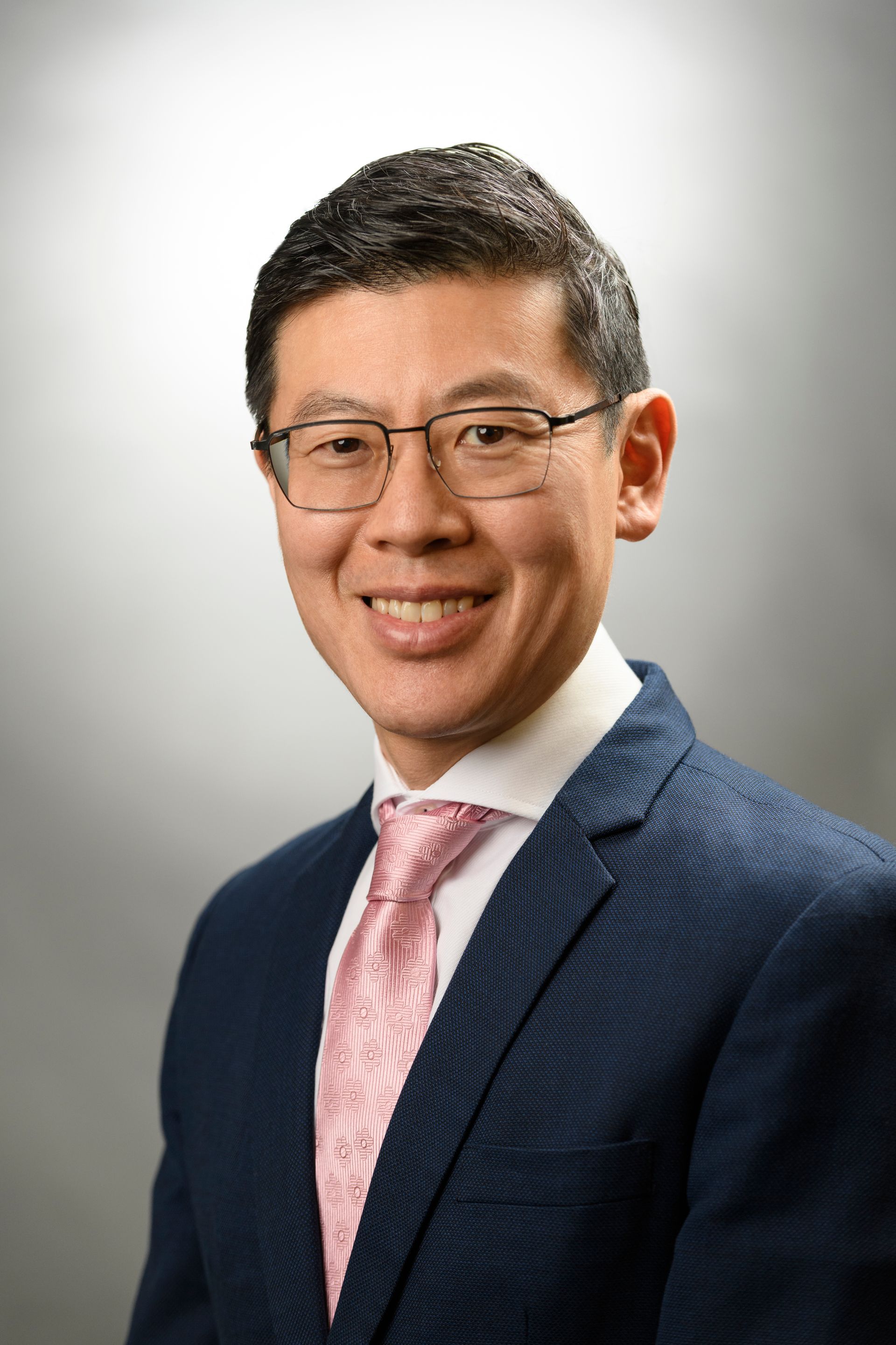 Man wearing glasses and blue scrubs smiles in a medical setting.