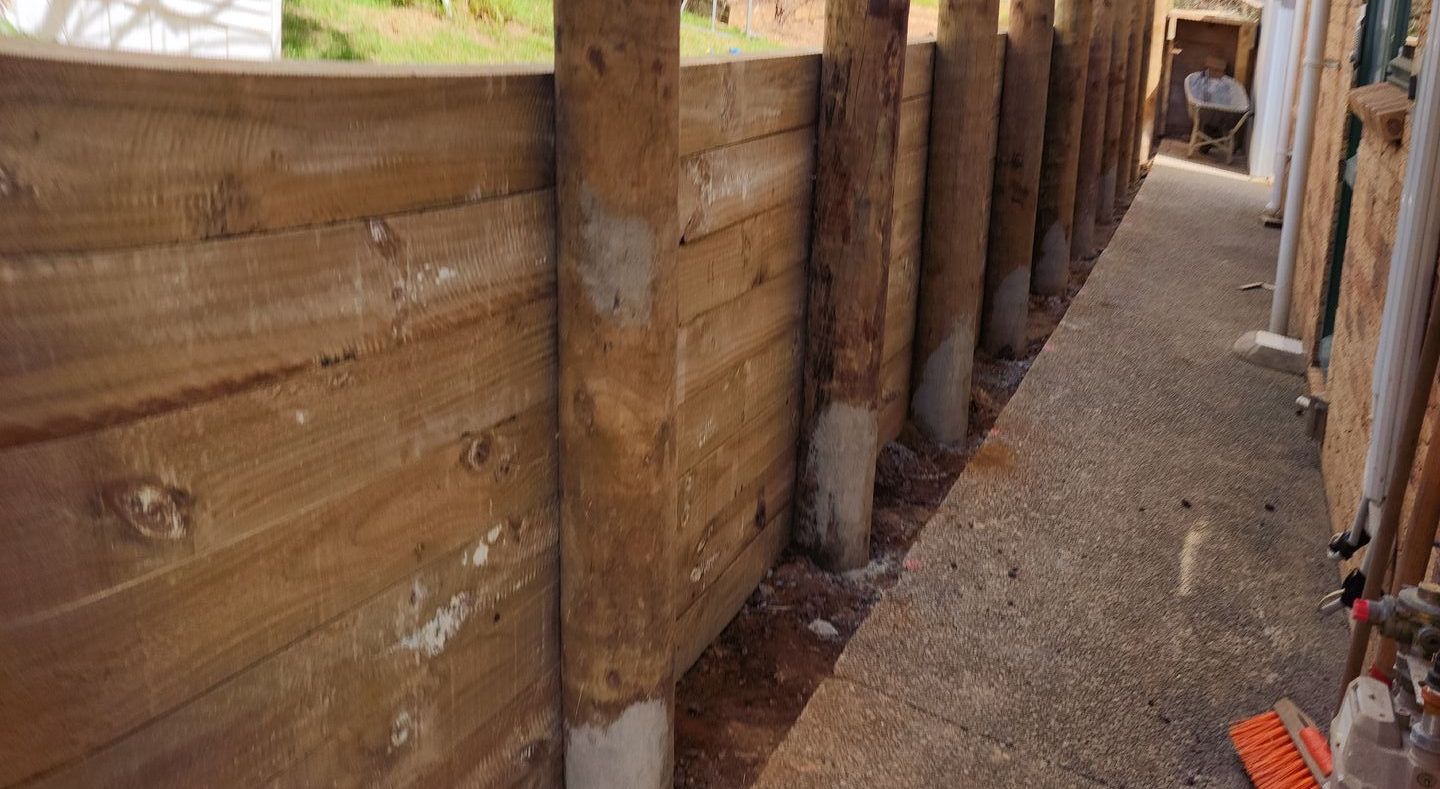 Wooden retaining wall construction with vertical posts and horizontal planks. Concrete base and narrow pathway.
