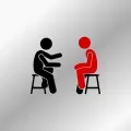 Two people are sitting on stools talking to each other.