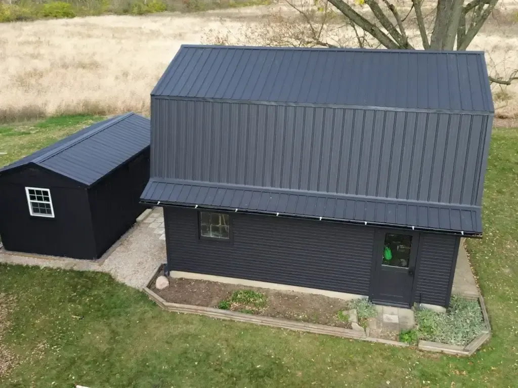 An aerial view of a black barn and shed in a grassy field.