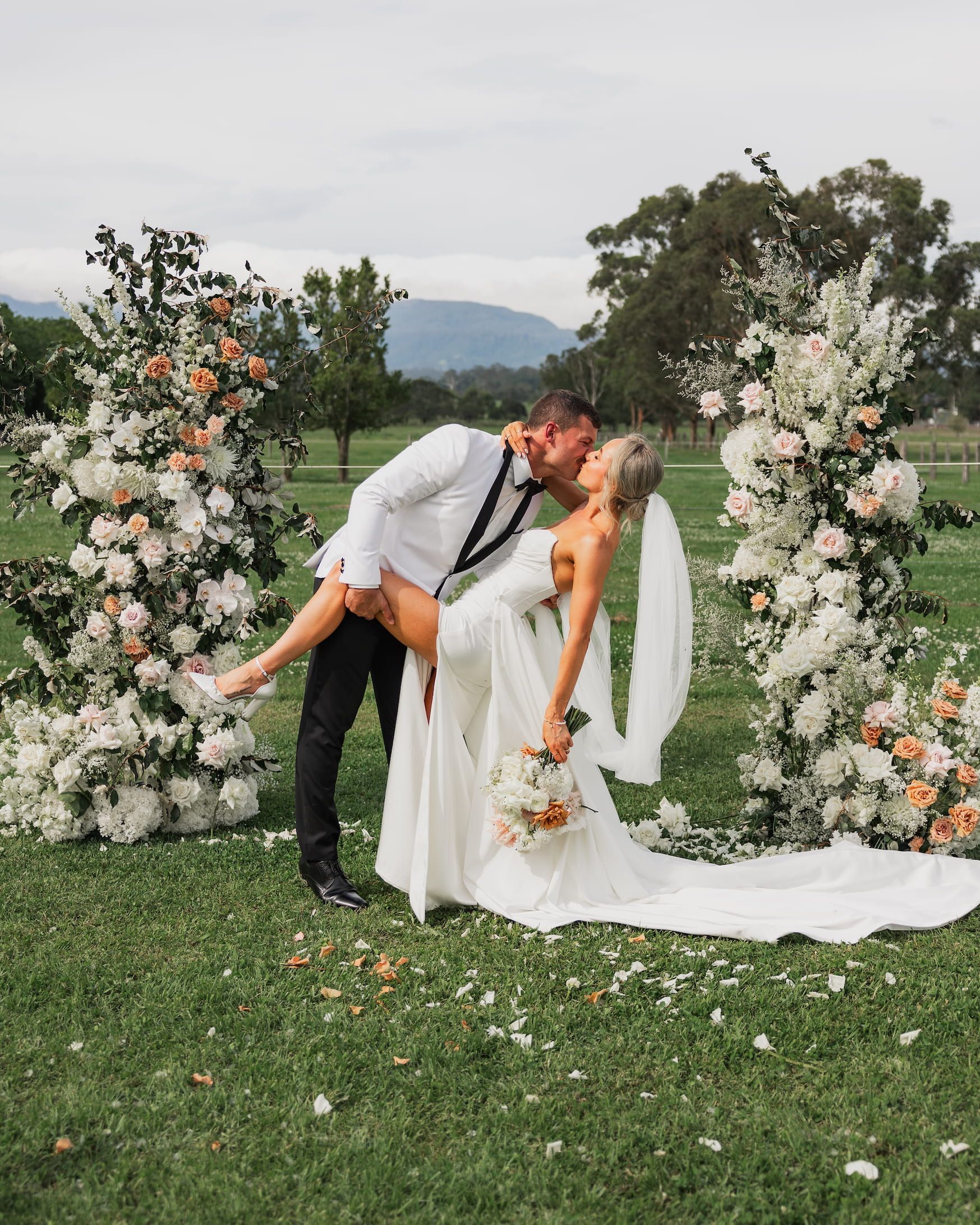 Bride and groom are standing in front of a floral — Flowers in Fairy Meadow, NSW
