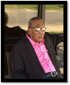 A man in a suit and pink shirt is sitting in a chair.