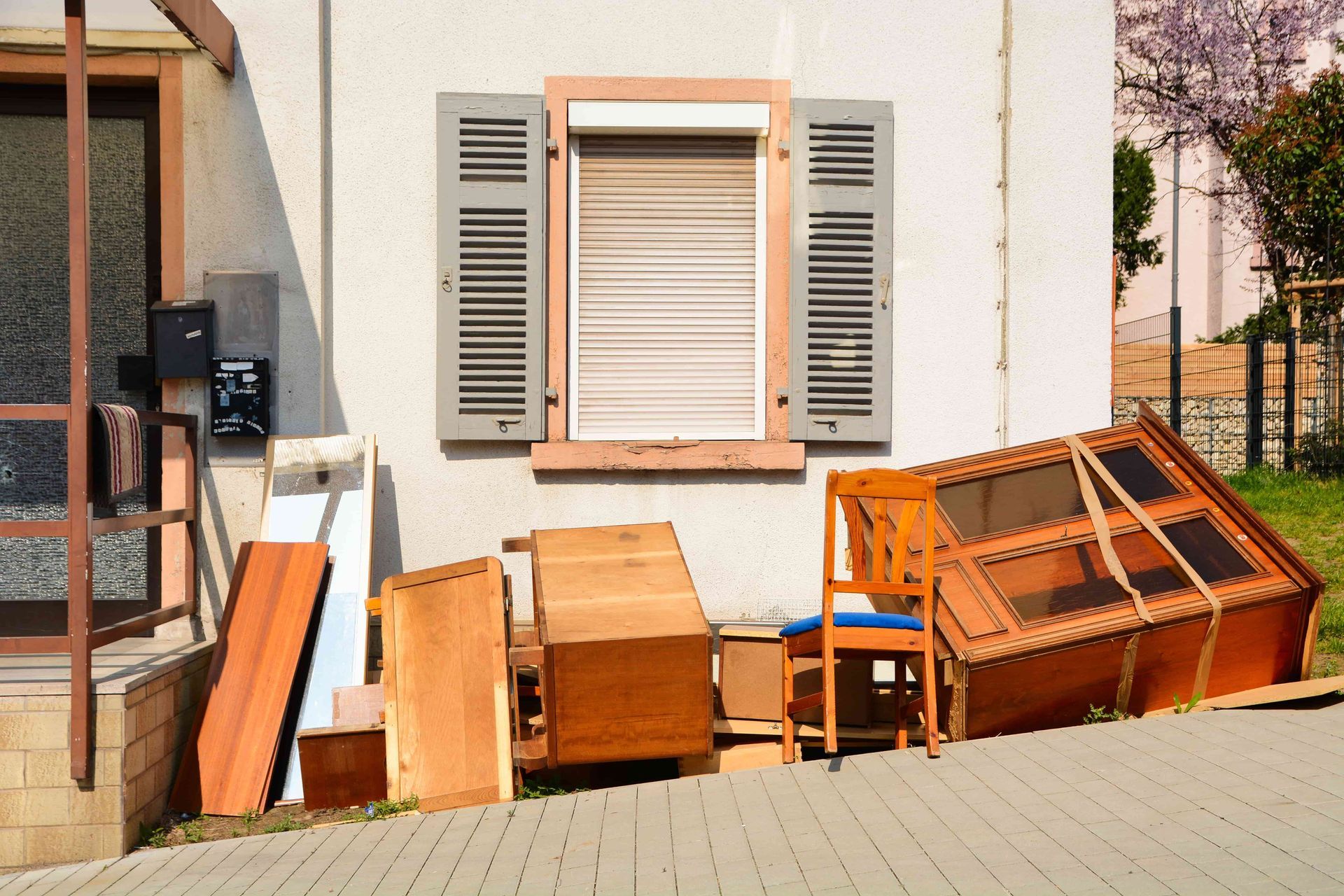 Furniture piled outside a building with closed shutters; sunny day.