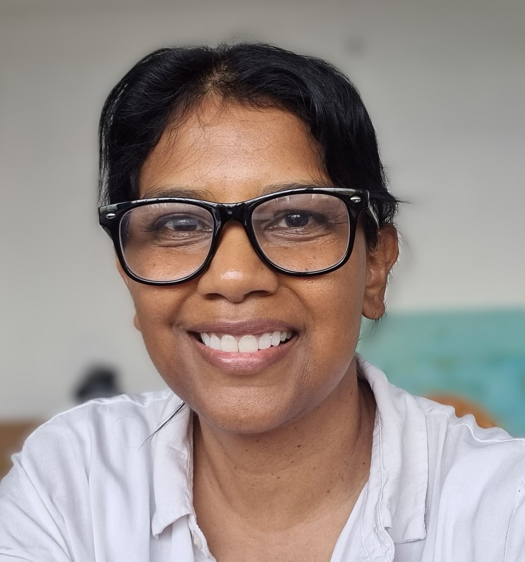 Woman with glasses smiles at the camera, wearing a light-colored shirt.