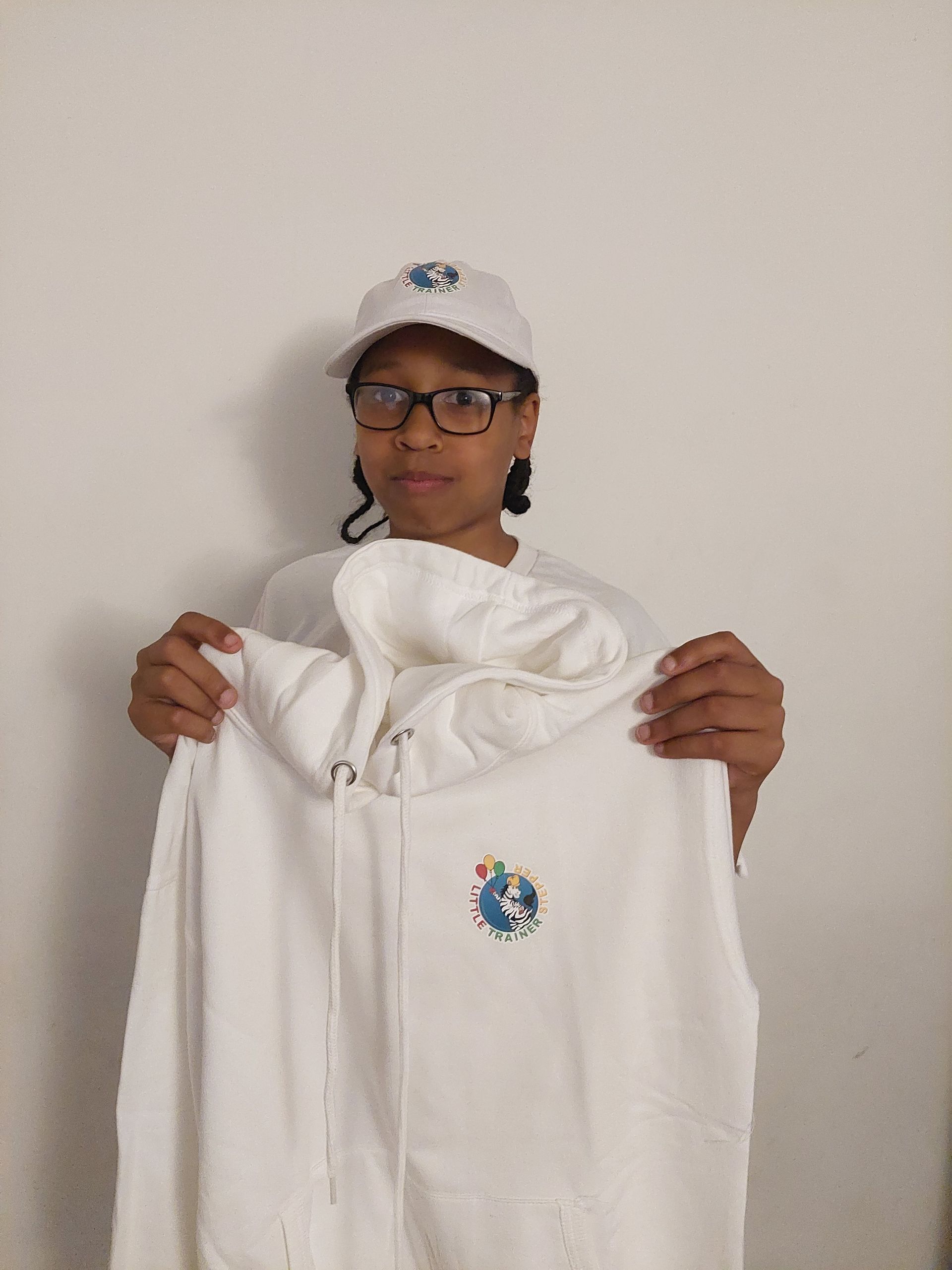 A woman wearing glasses and a hat is holding a white hoodie.