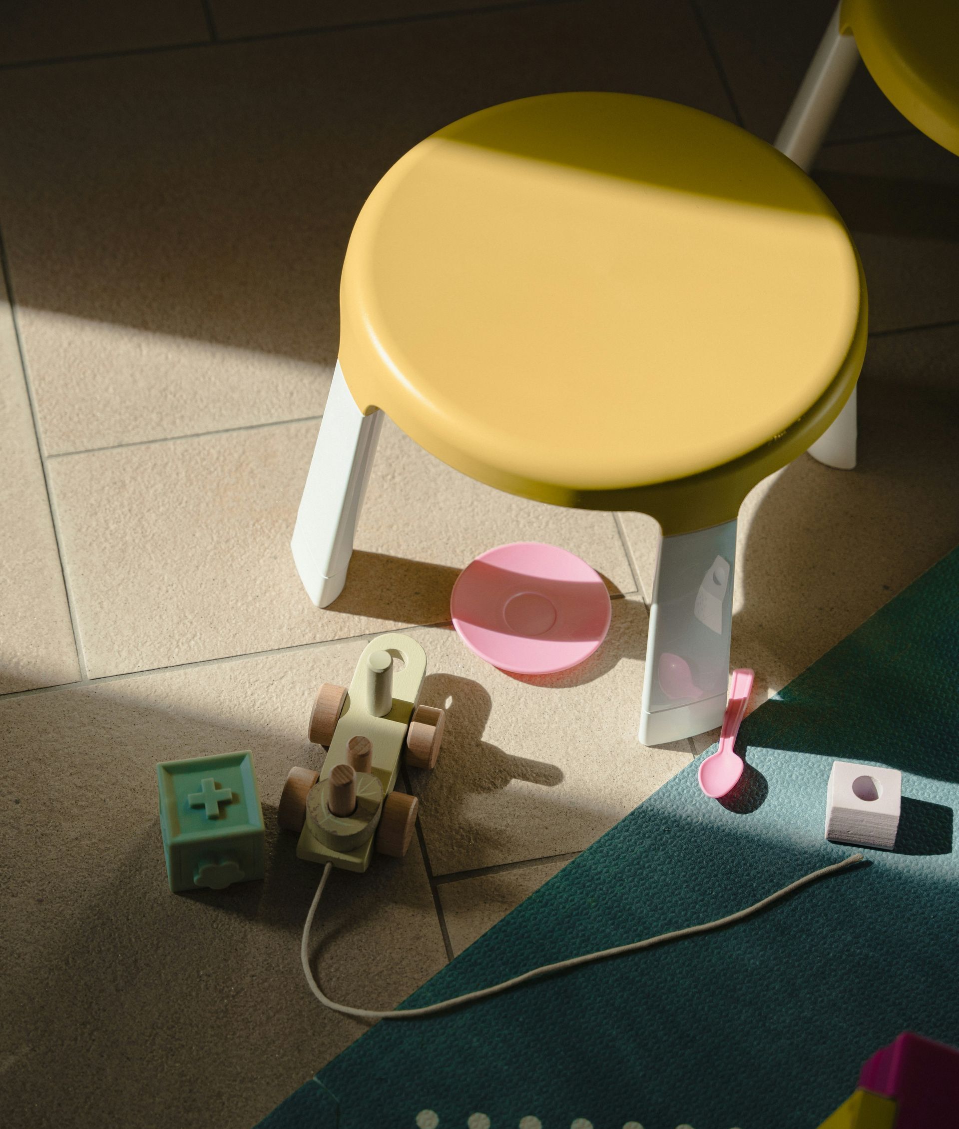 A yellow stool sits on a tiled floor next to a toy car