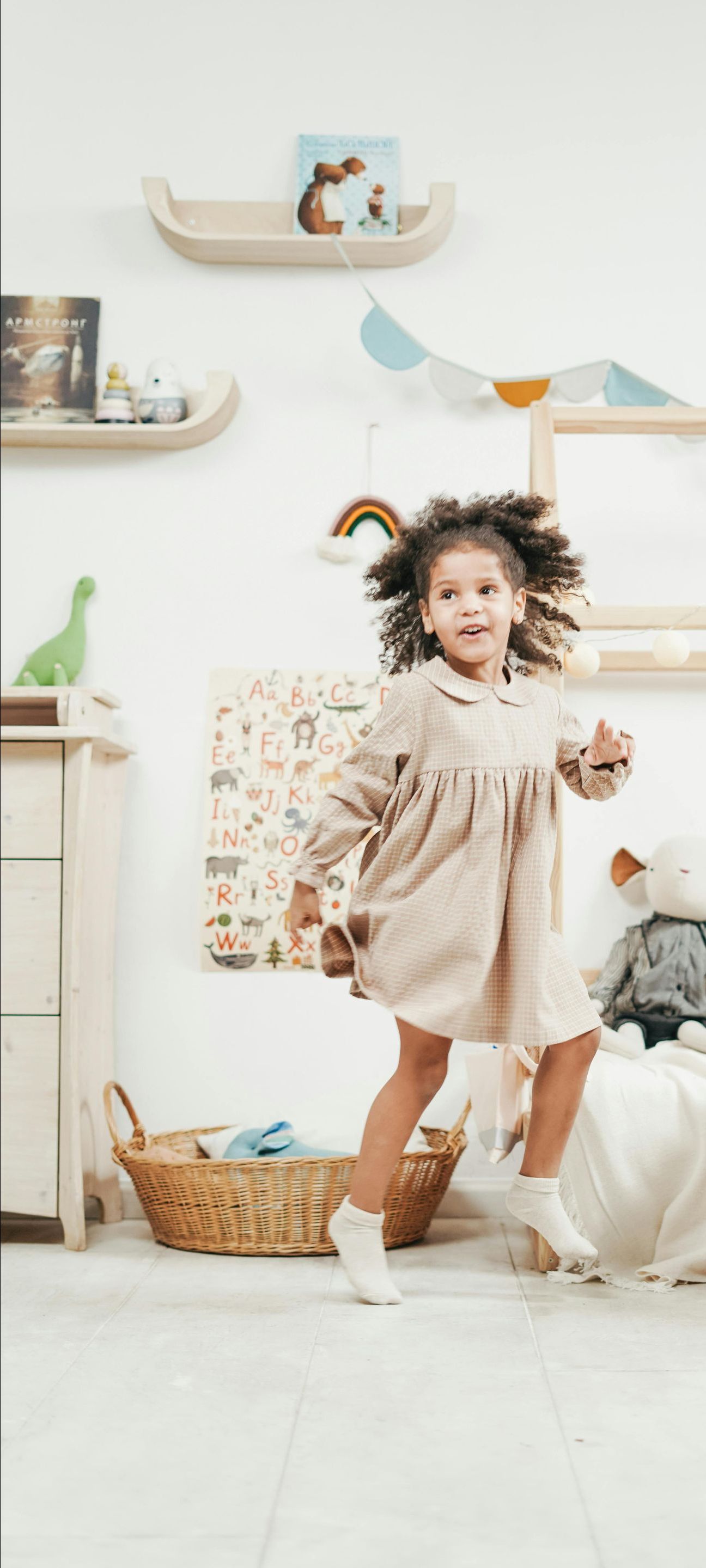 A little girl in a dress is jumping in the air in a room.