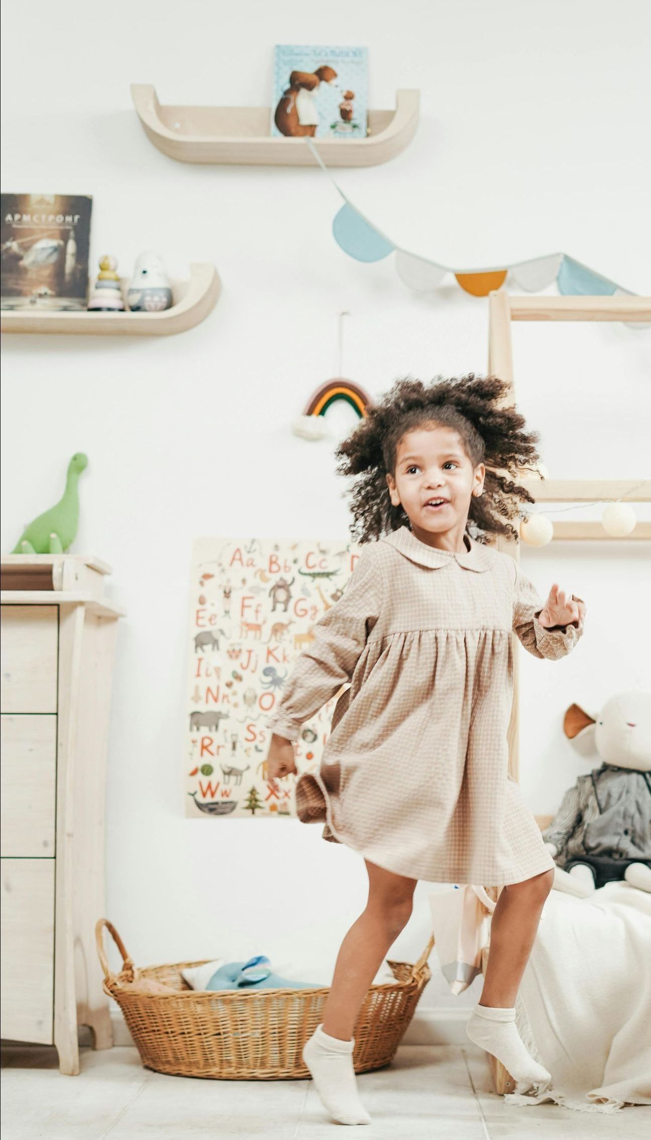 A little girl in a dress is jumping in the air in a room.
