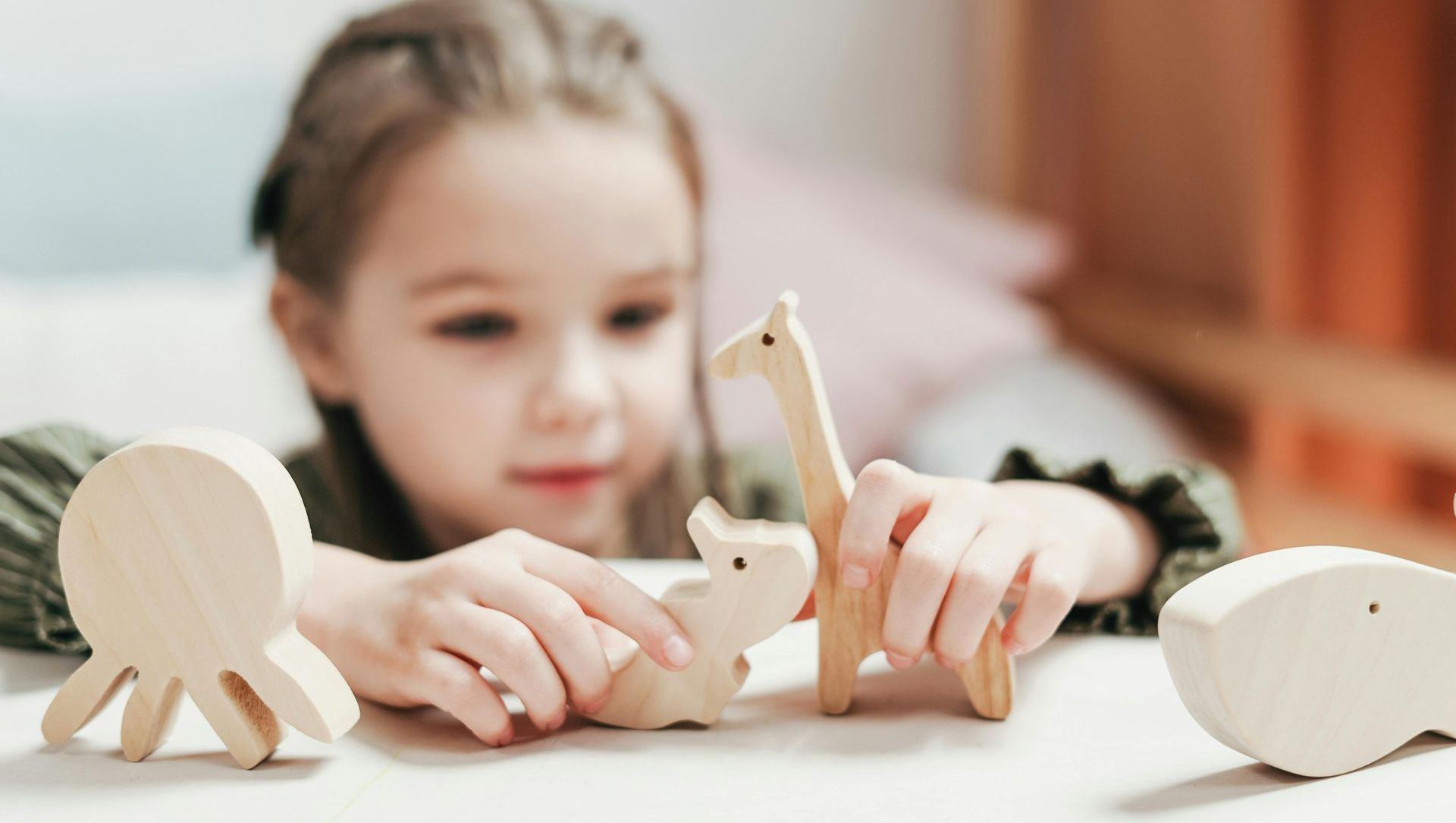 A little girl is playing with wooden animals on a table.