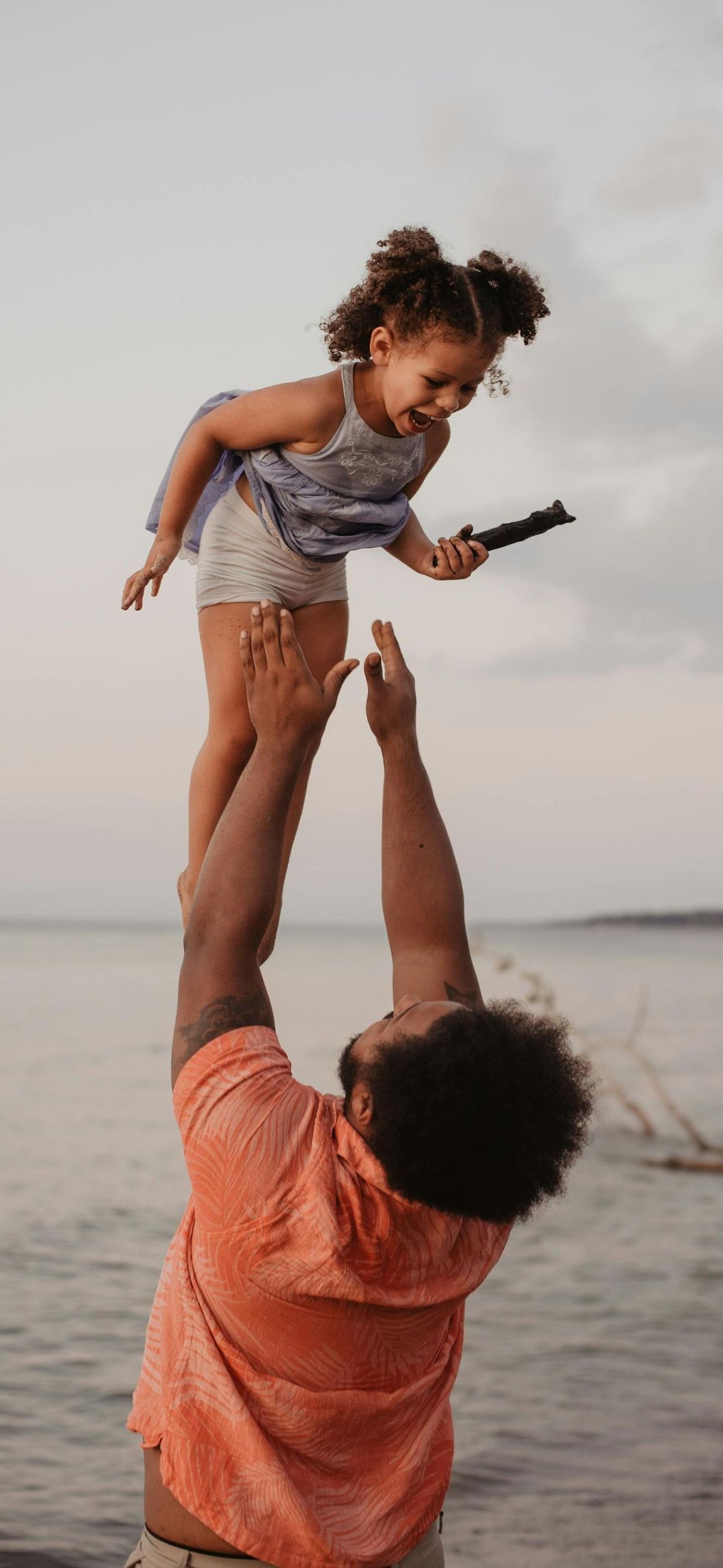 A man is holding a little girl in the air on the beach.