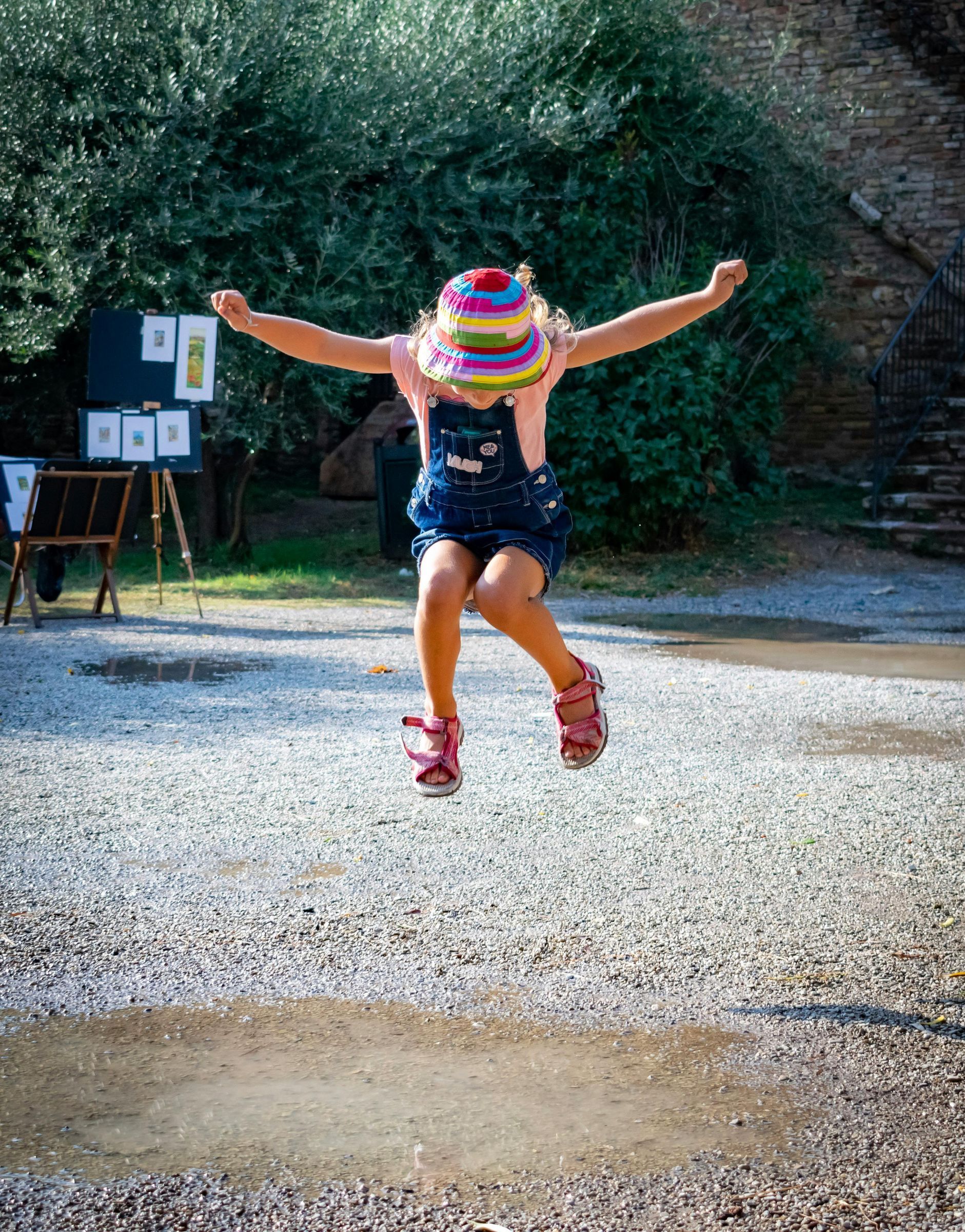 A little girl is jumping in the air with her arms outstretched.