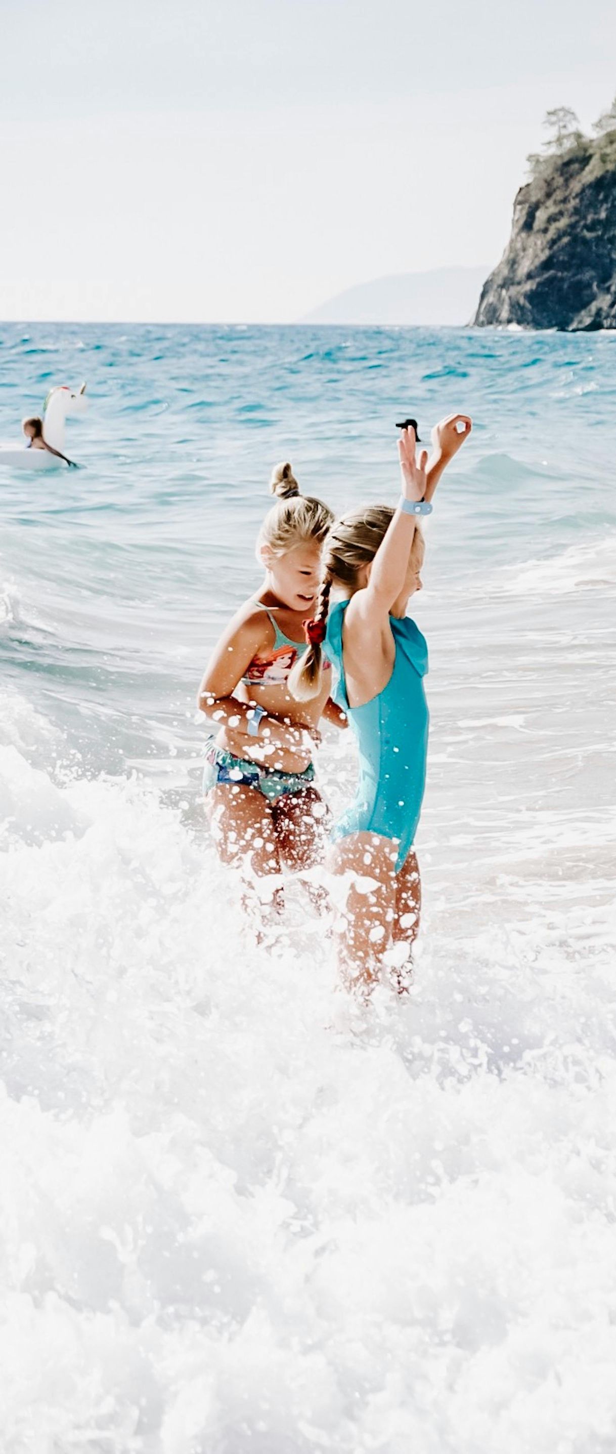 Two young girls are playing in the ocean on a beach.